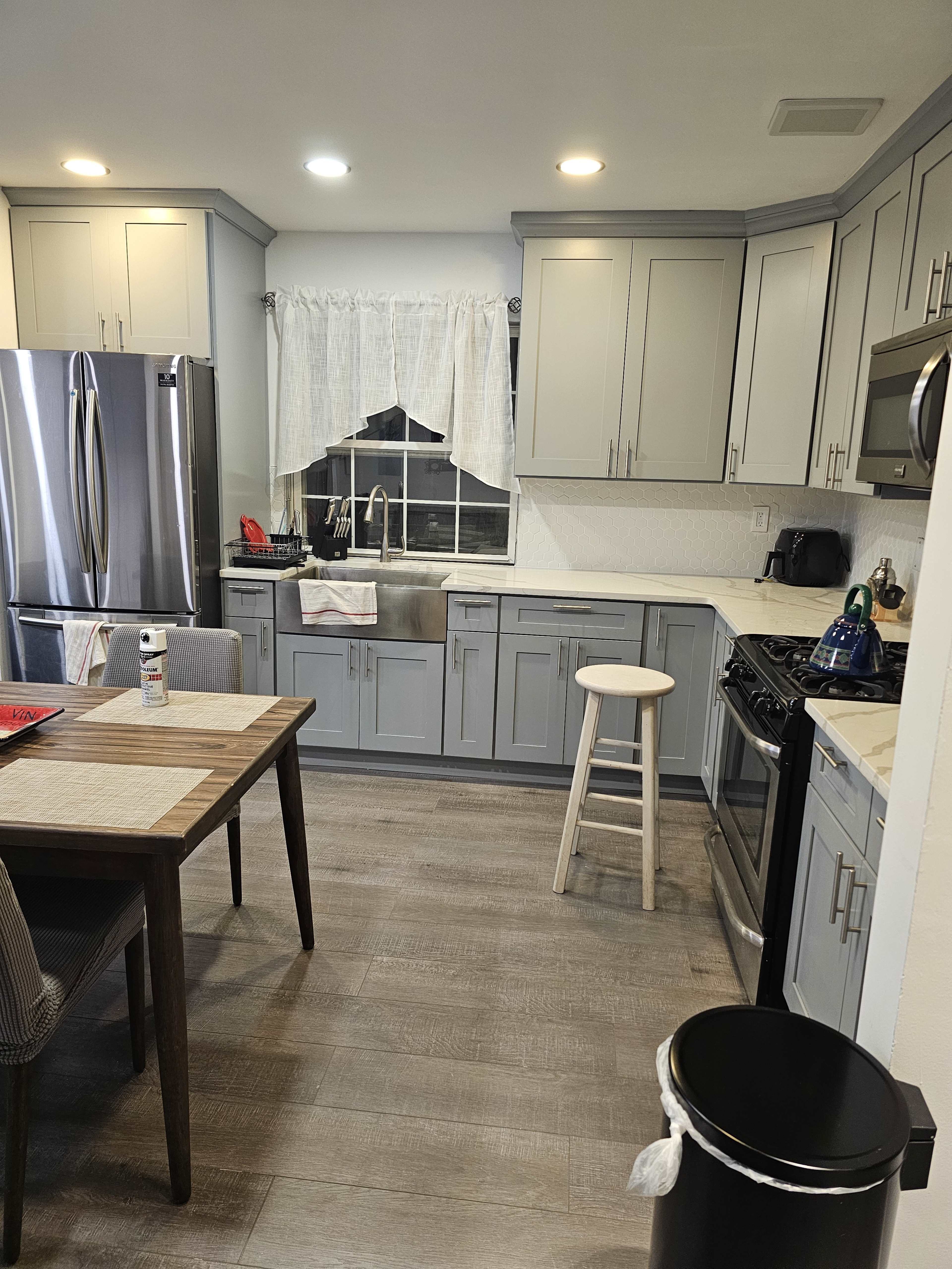 A modern kitchen with gray cabinets, a stainless steel refrigerator, a dining table, and a stool placed near the counter.