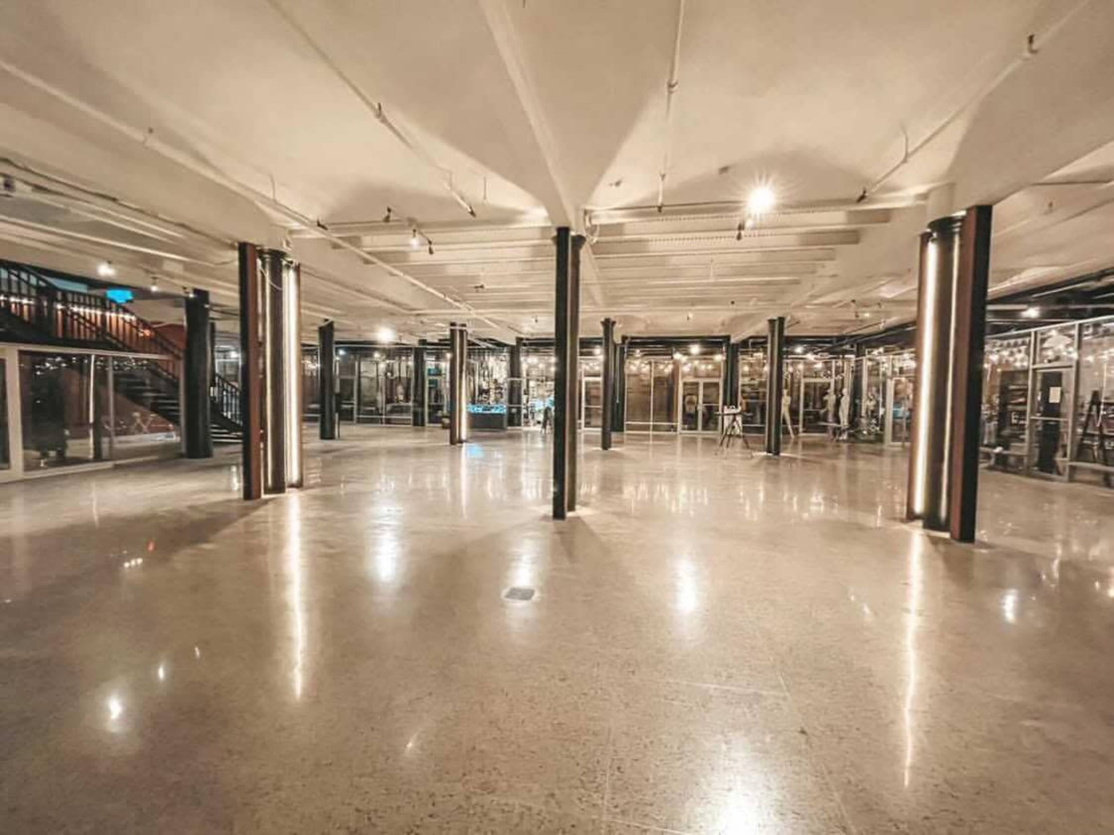 A spacious, empty interior with polished concrete flooring and several columns, illuminated by overhead lights.