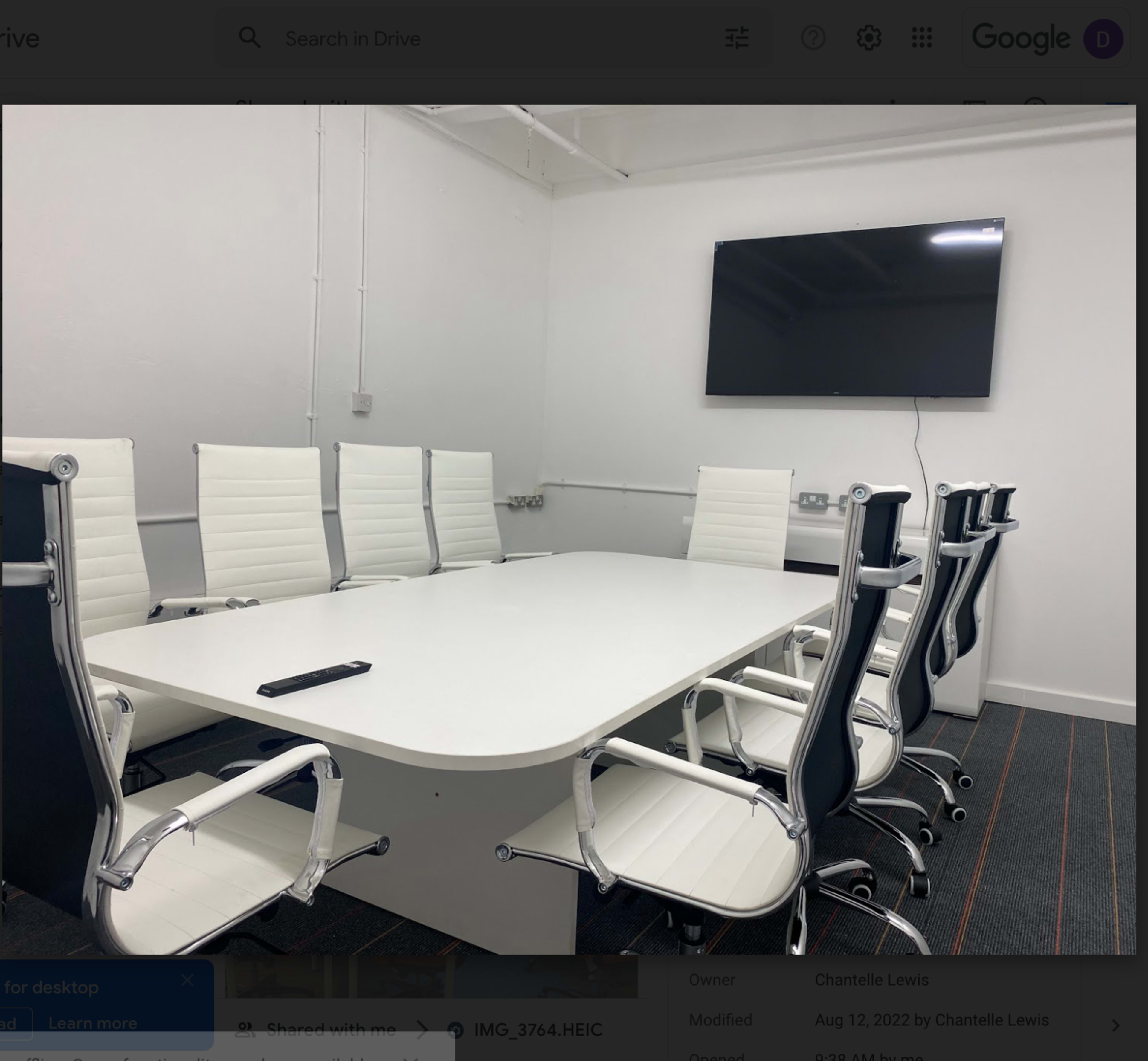 A modern conference room with a large white table surrounded by several sleek, white office chairs and a wall-mounted television.