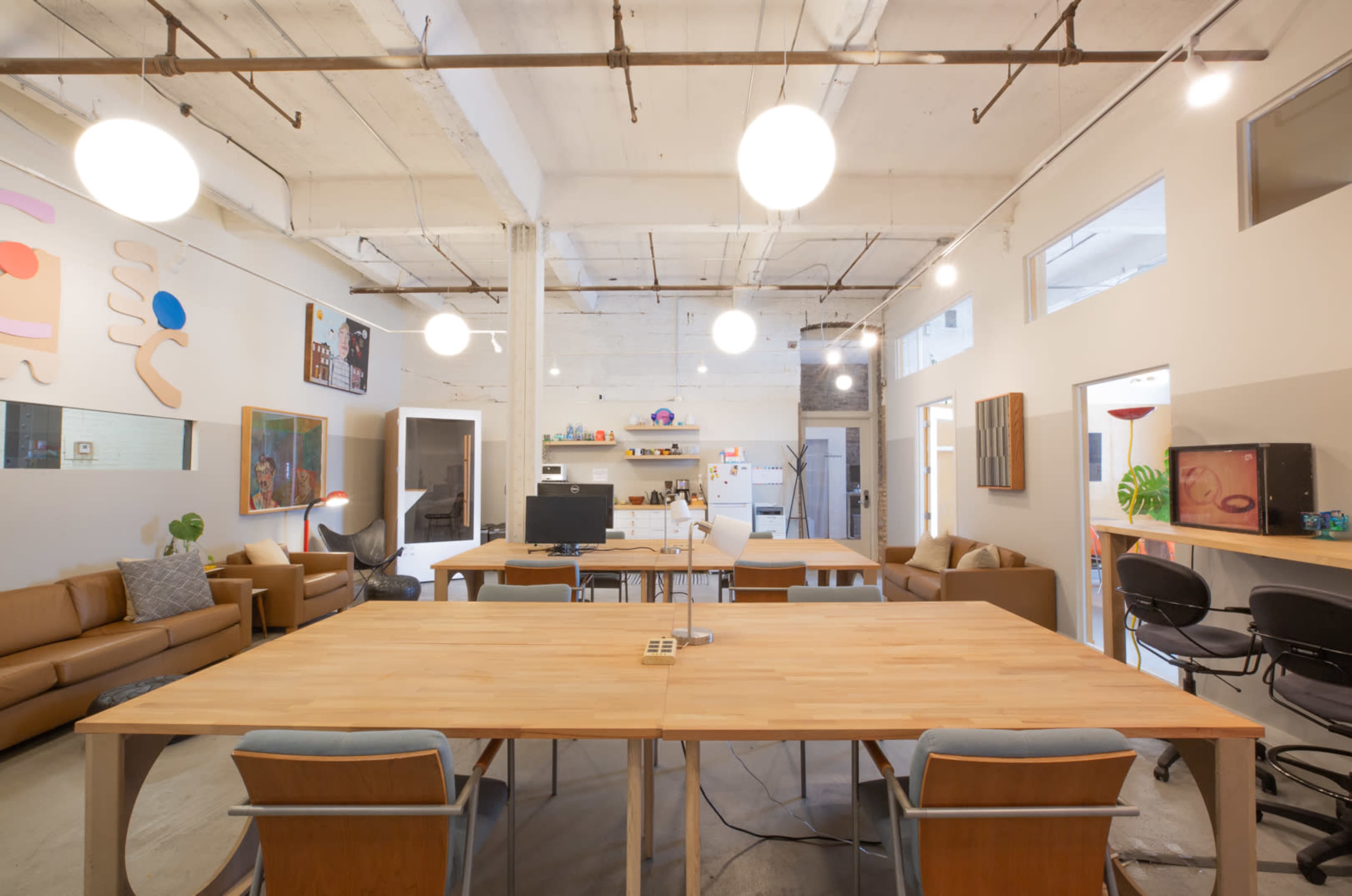 A spacious, modern office features large wooden tables, comfortable seating areas, and bright overhead lights.