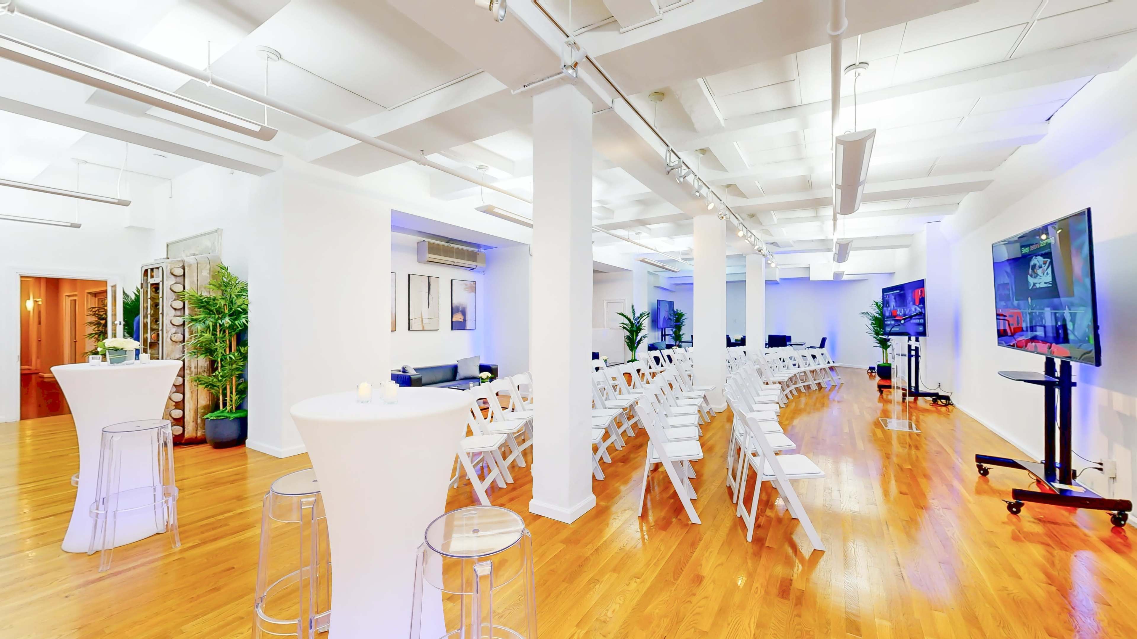 The image shows a spacious event venue with white folding chairs arranged in rows facing a display screen, and additional tall tables positioned around the area.