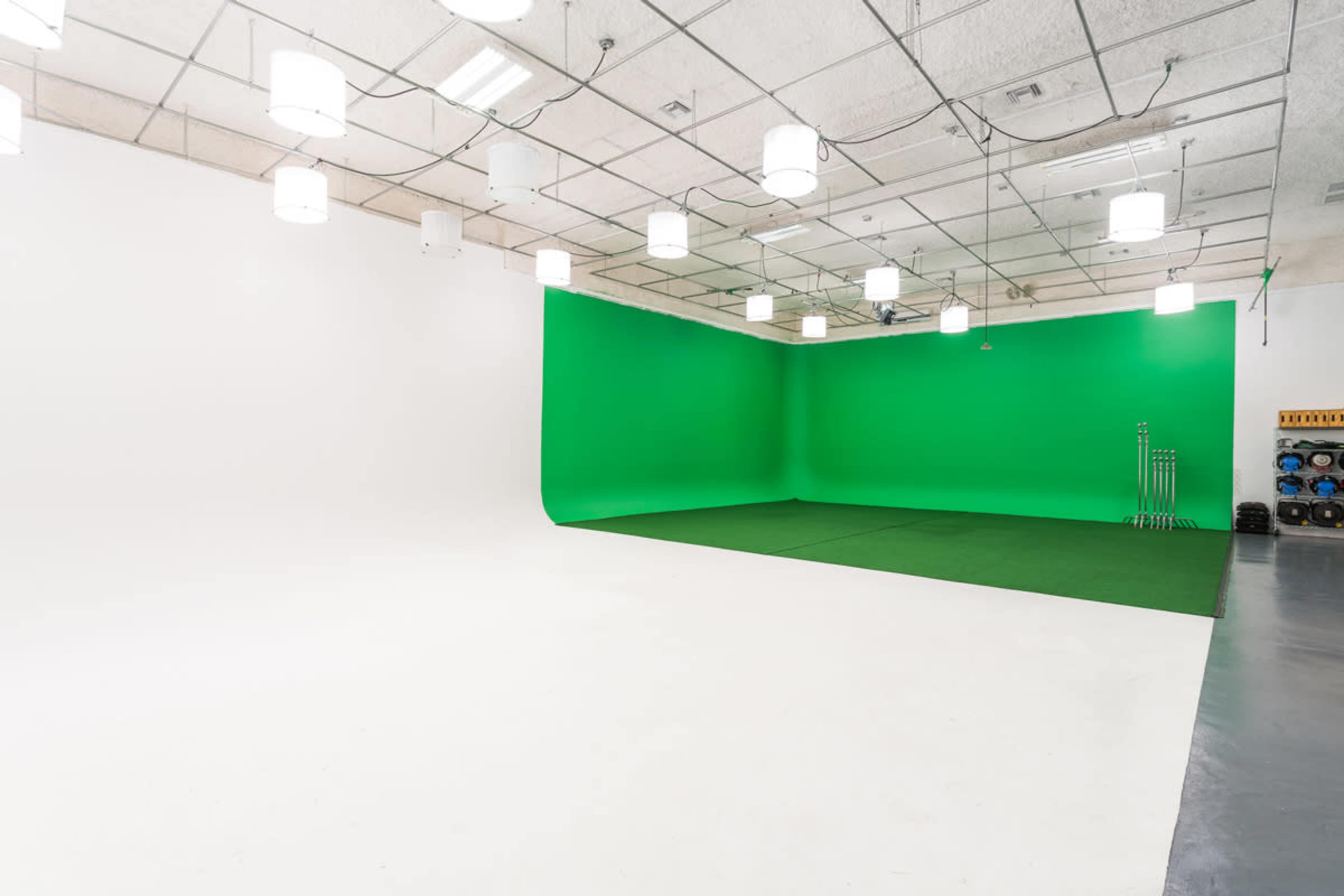 A spacious studio featuring a green screen background, white walls, and a clean, well-lit floor area.