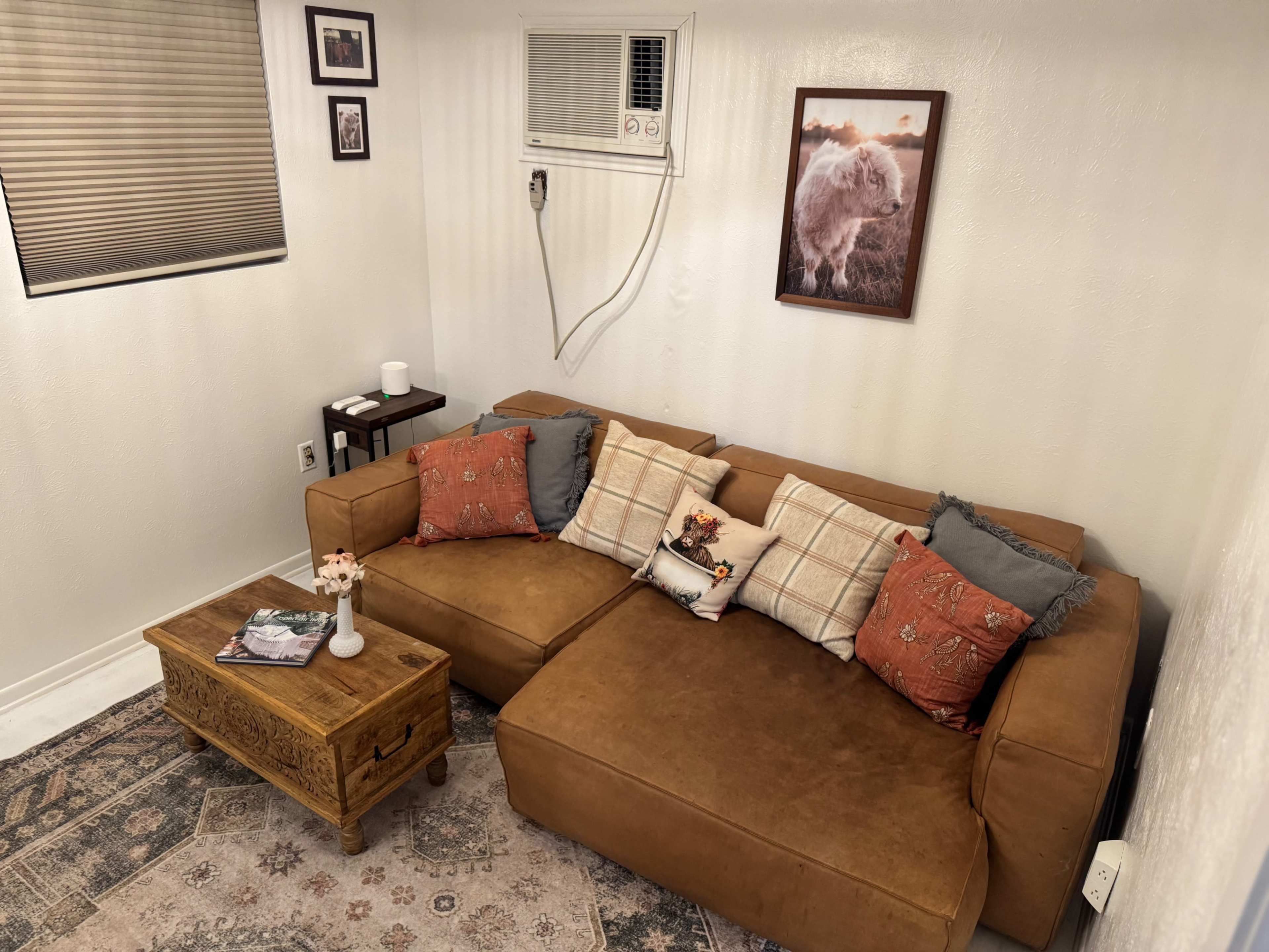 A cozy living area features a brown sectional sofa adorned with patterned cushions, a wooden coffee table, and a wall-mounted air conditioning unit.