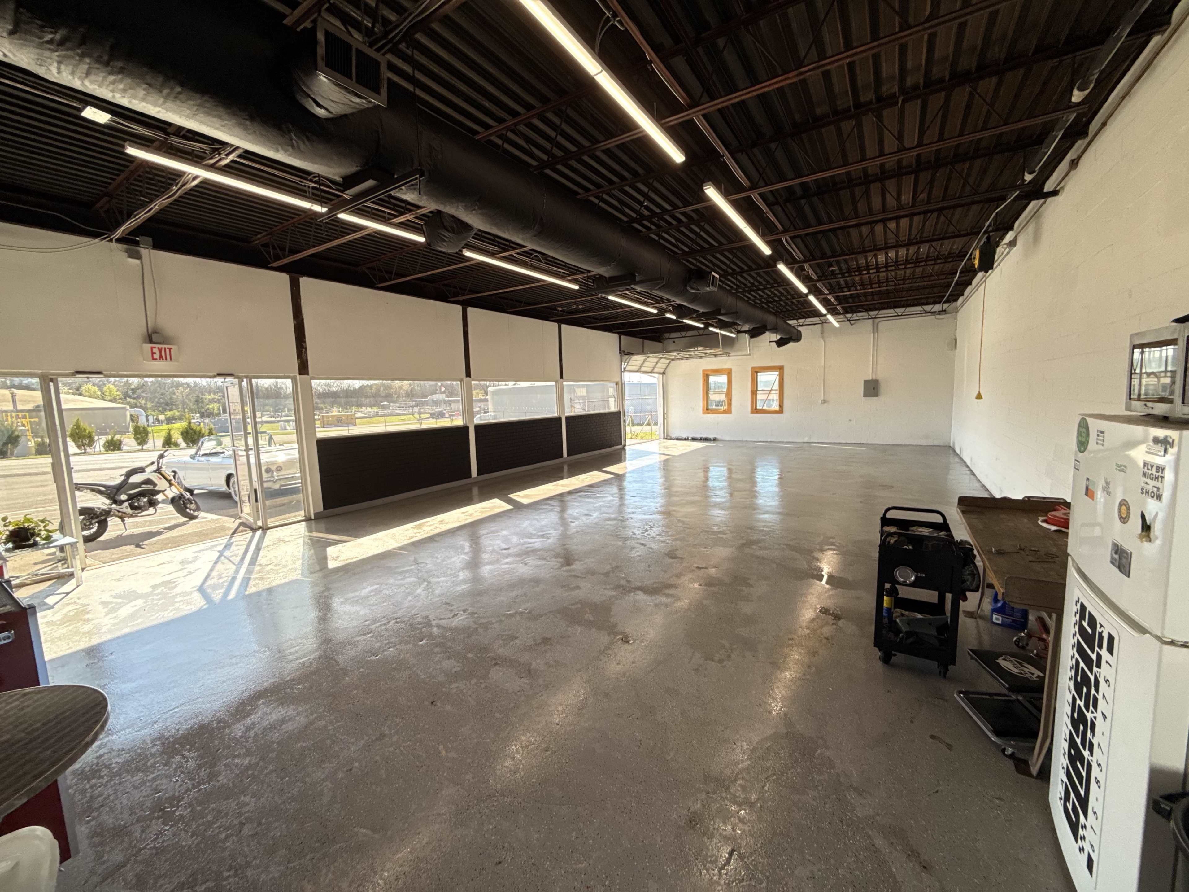 The image shows an empty industrial space with polished concrete floors, exposed beams, and large windows letting in natural light.