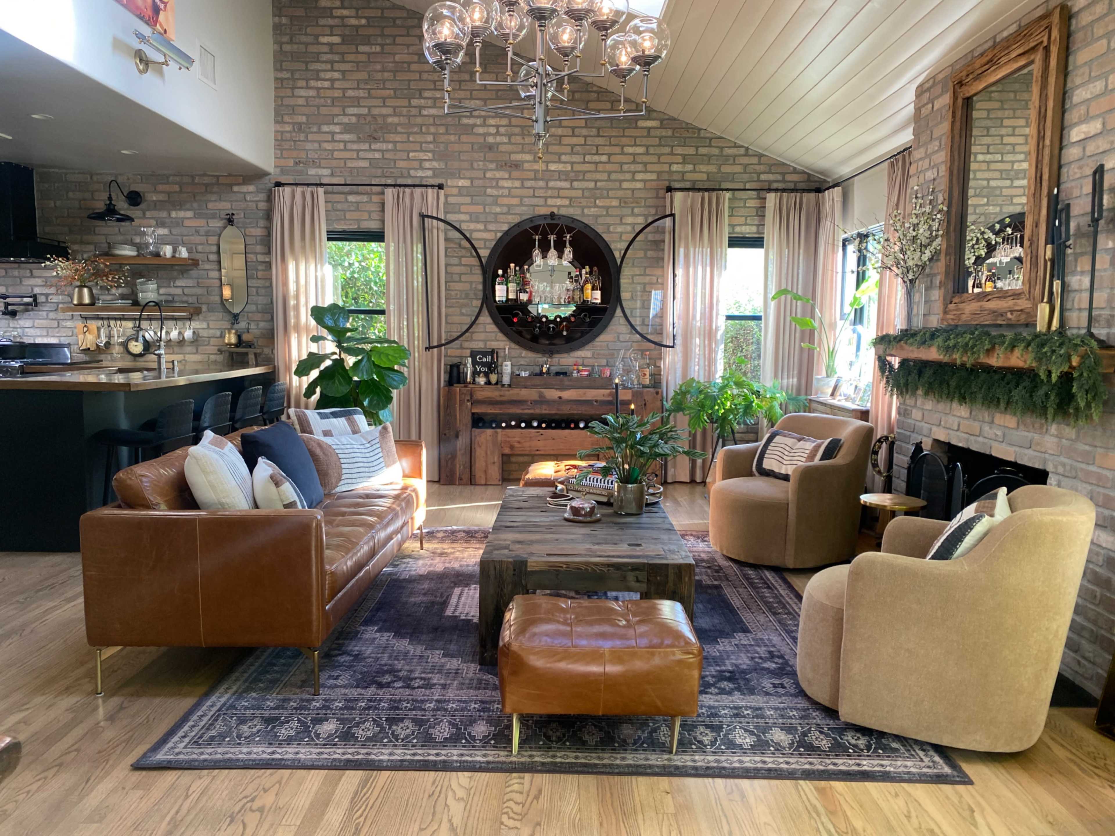 A modern living room features a mix of leather and fabric seating, a wooden coffee table, and a stone wall, with plants and a chandelier adding style.