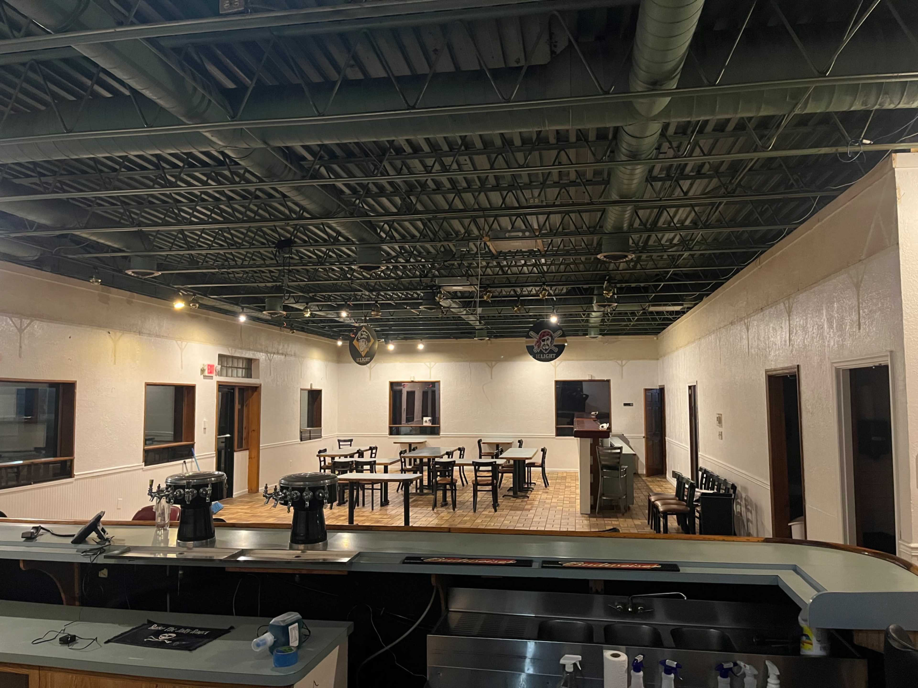 The image shows an empty restaurant interior with rows of tables and a bar area in the foreground.