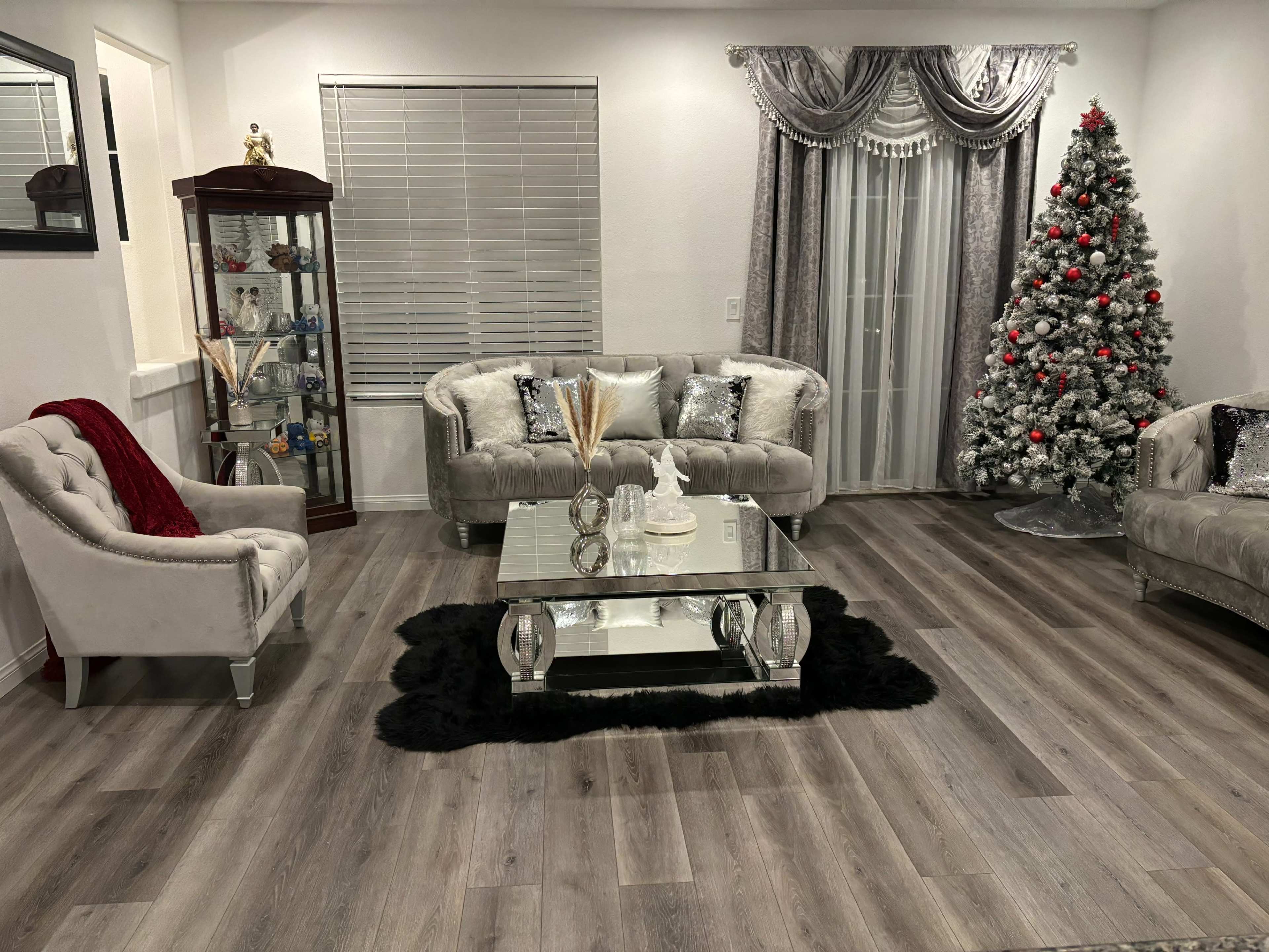 The image shows a elegantly decorated living room featuring plush sofas, a glass coffee table, and a Christmas tree adorned with lights and ornaments.