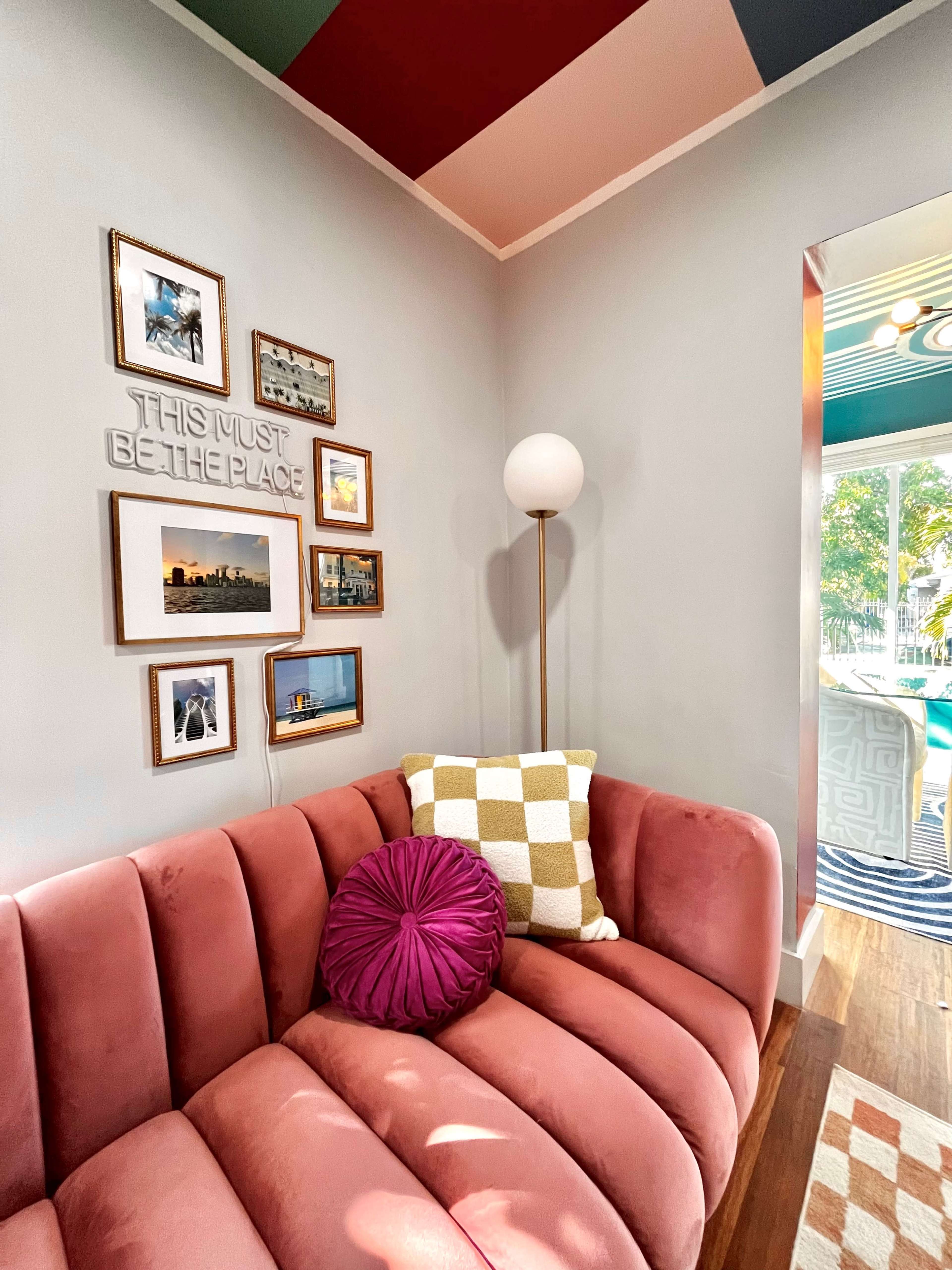 This image features a cozy corner with a curved pink sofa, adorned with decorative pillows, a modern floor lamp, and a gallery wall of framed photographs.