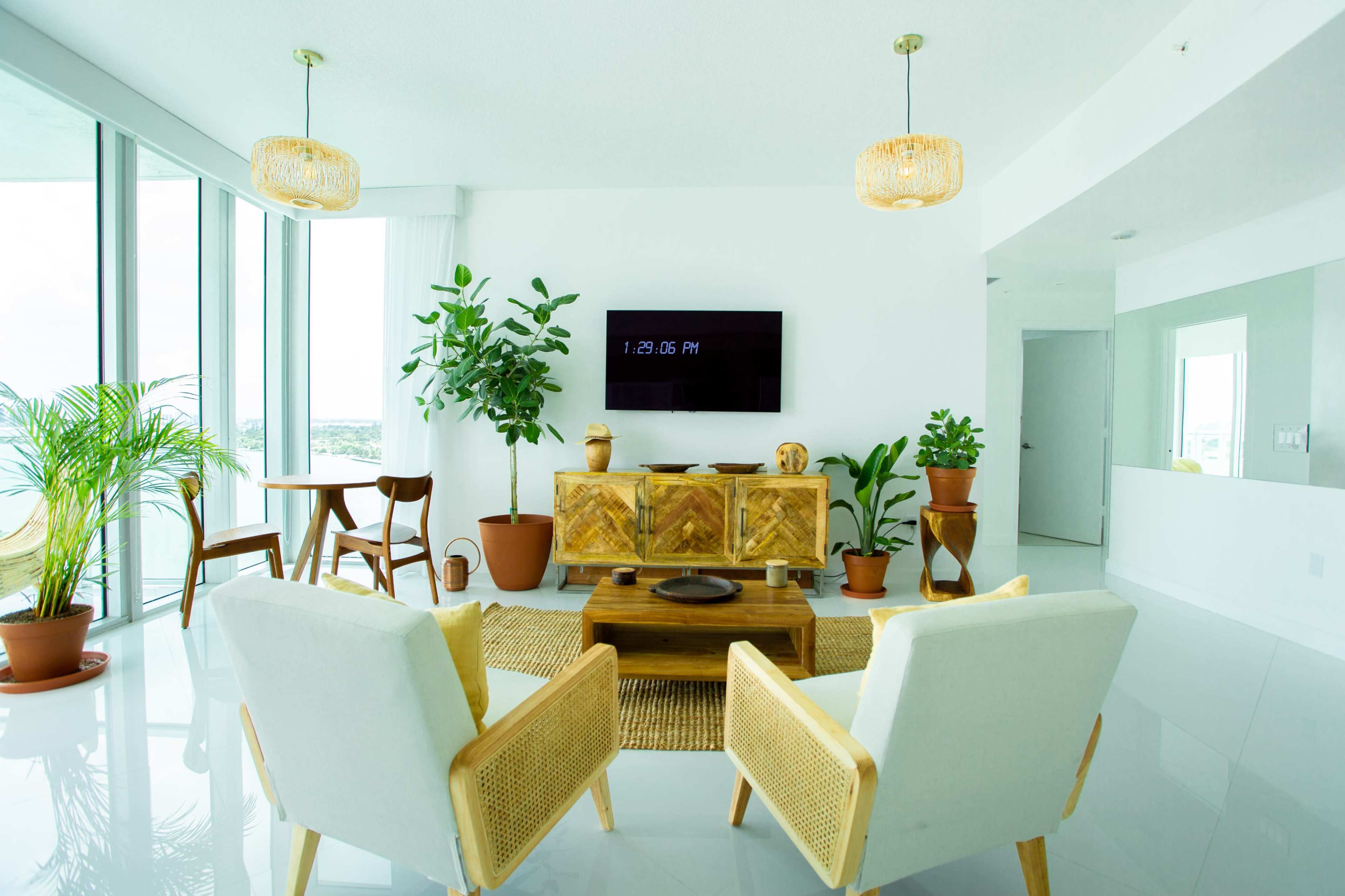 A modern living space features two armchairs facing a wooden coffee table, flanked by potted plants and a wall-mounted television.