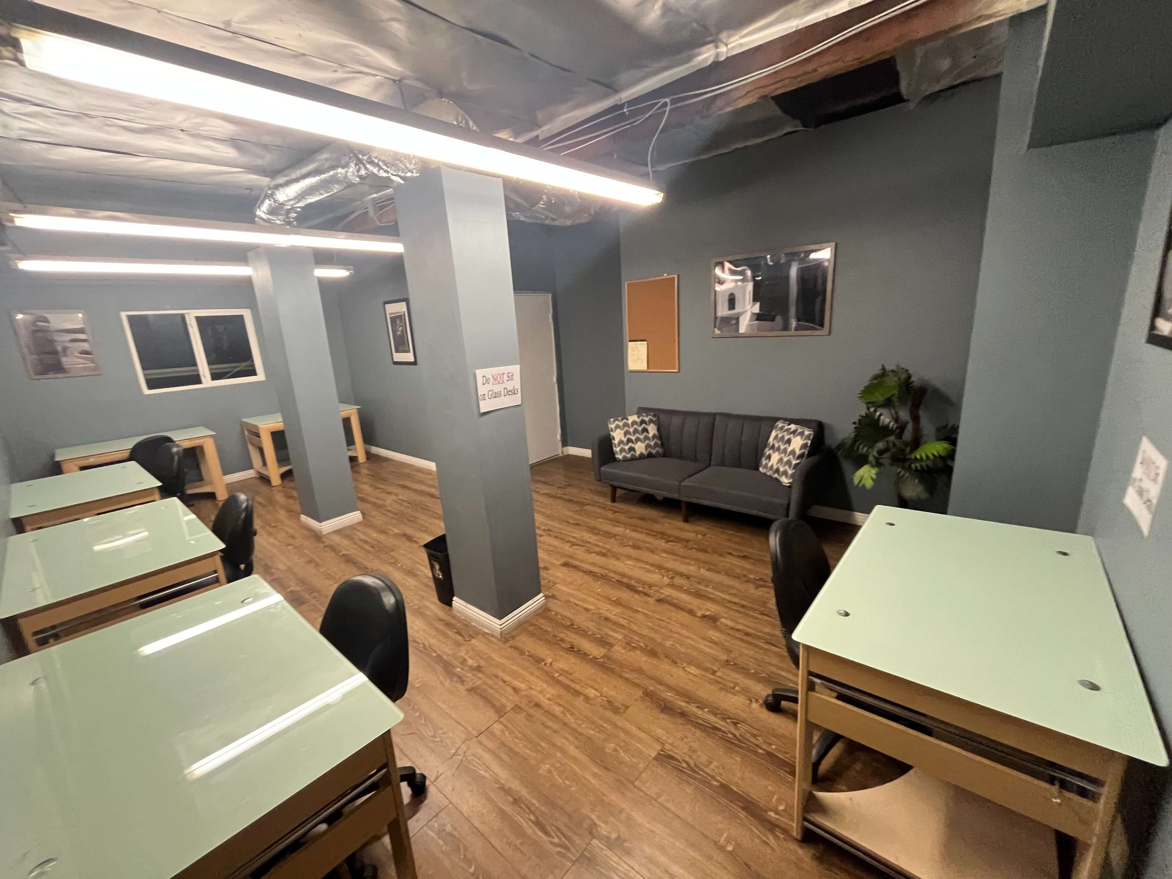 The image shows a room with several tables and chairs, a sofa in one corner, and gray-blue walls.