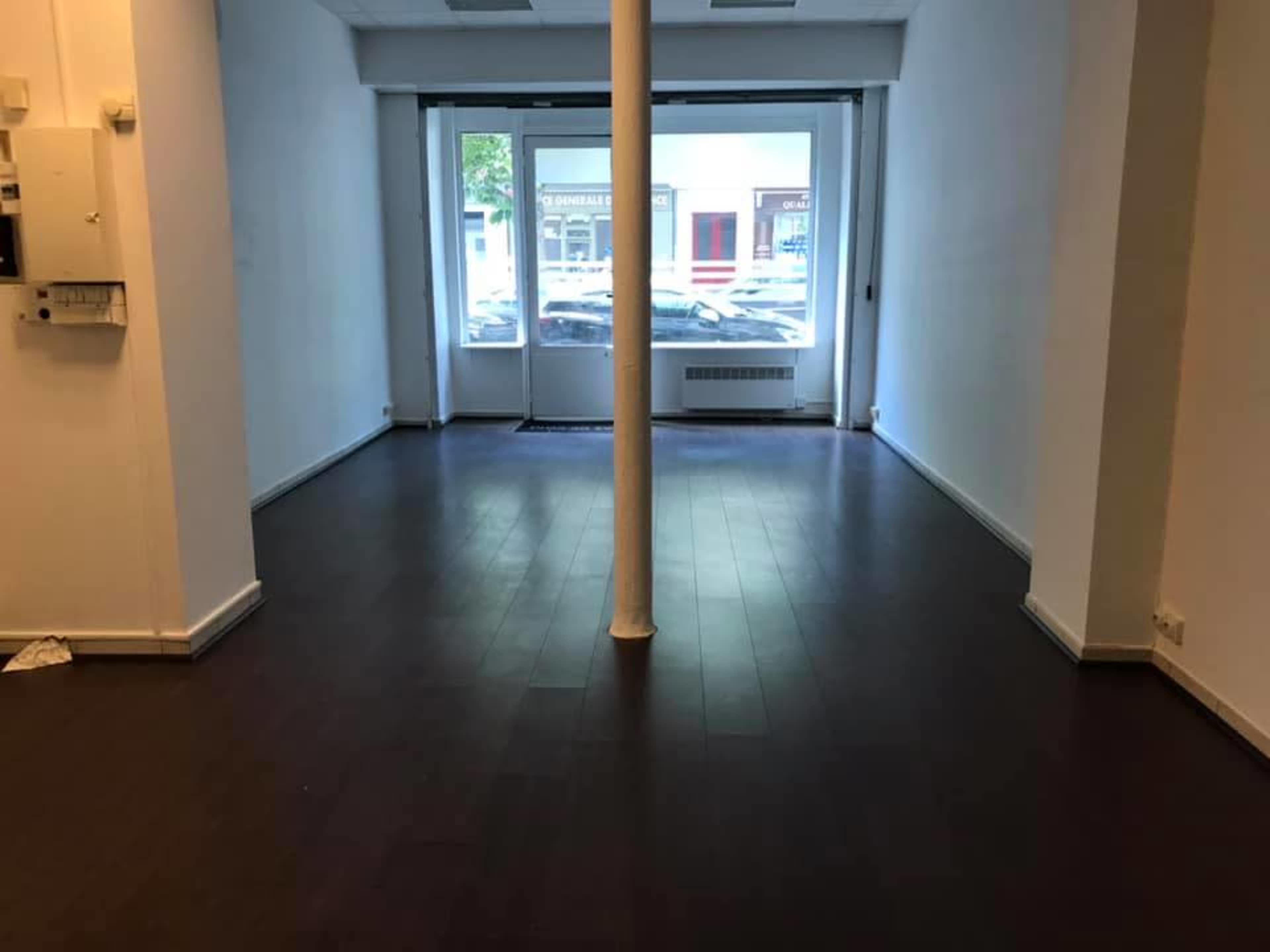 The image shows an empty retail space with dark wooden flooring and large windows at the front.