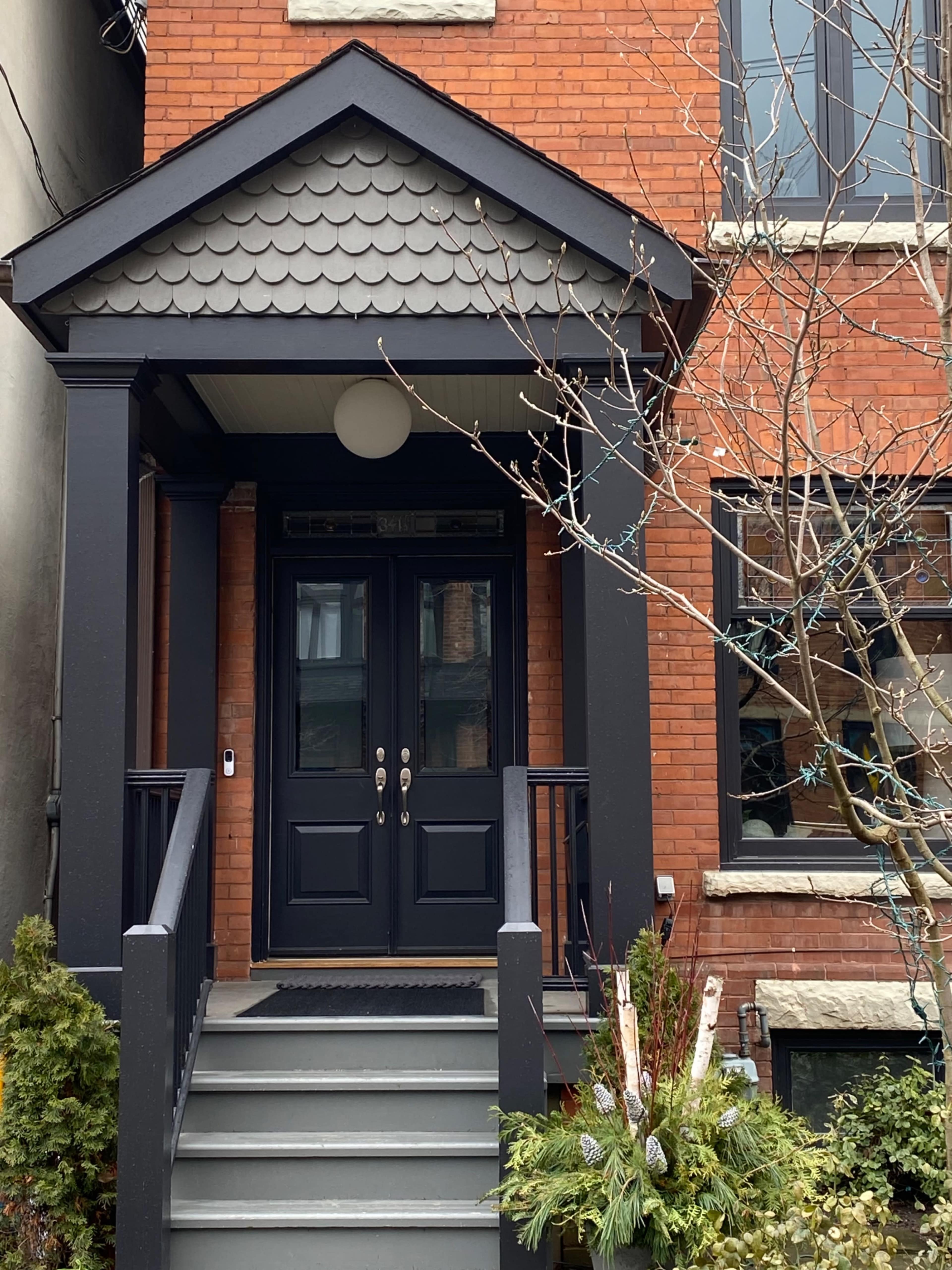 A brick house with a double front door under a gabled porch and a small set of steps leading to the entrance.