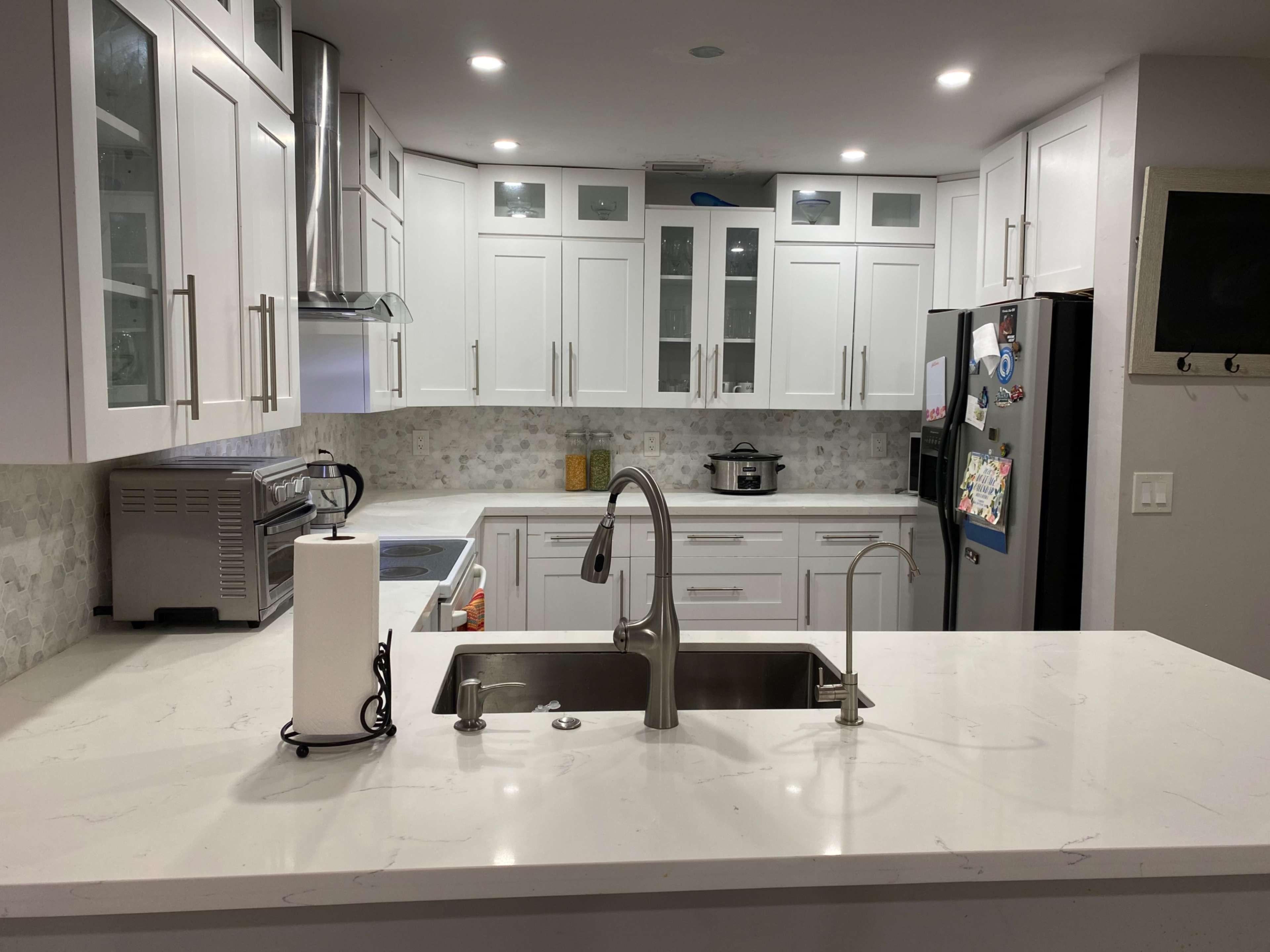 A modern kitchen features white cabinetry, stainless steel appliances, and a large island with a sink.