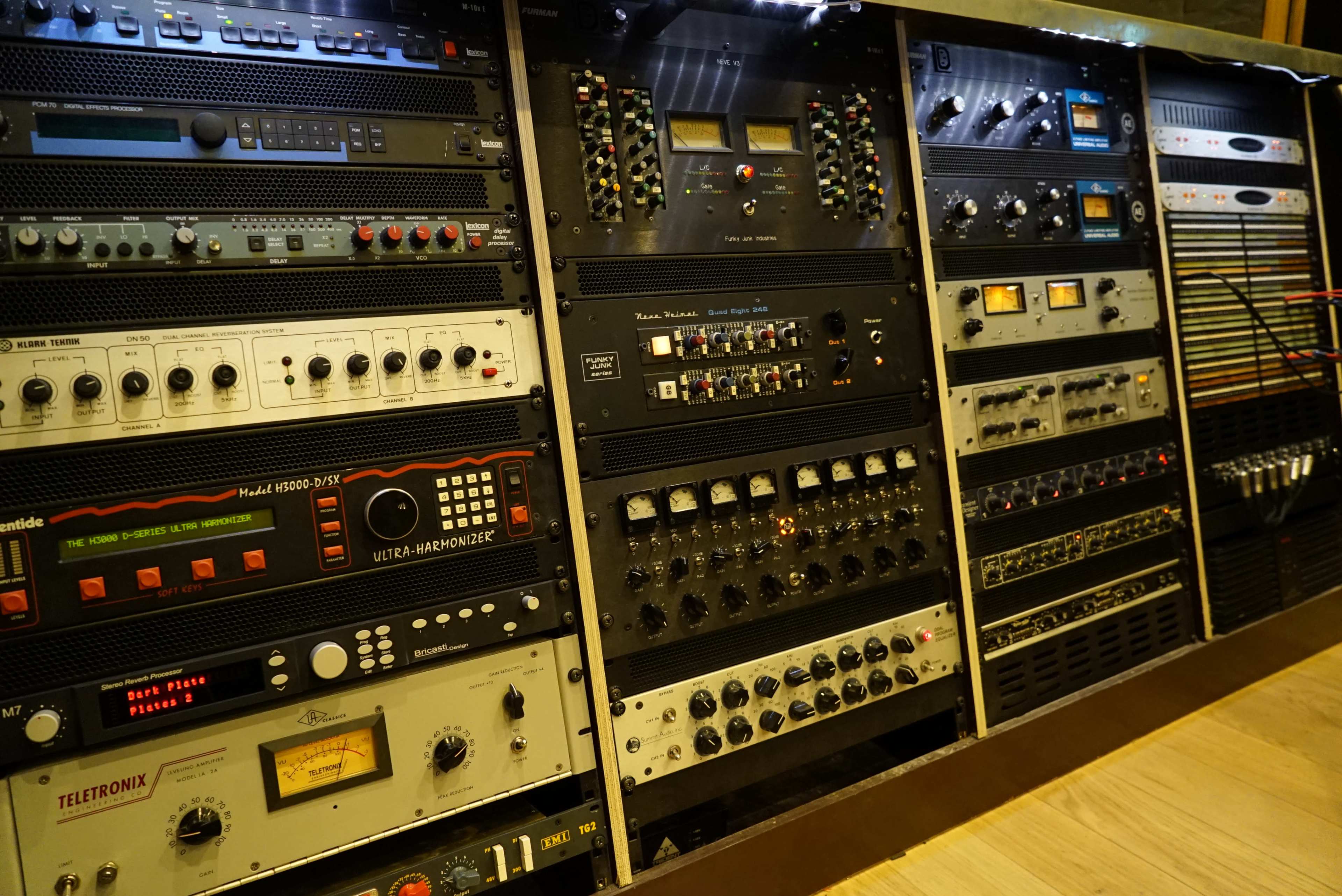 A wall of various audio equipment, including mixers, equalizers, and processors, organized in a studio setting.