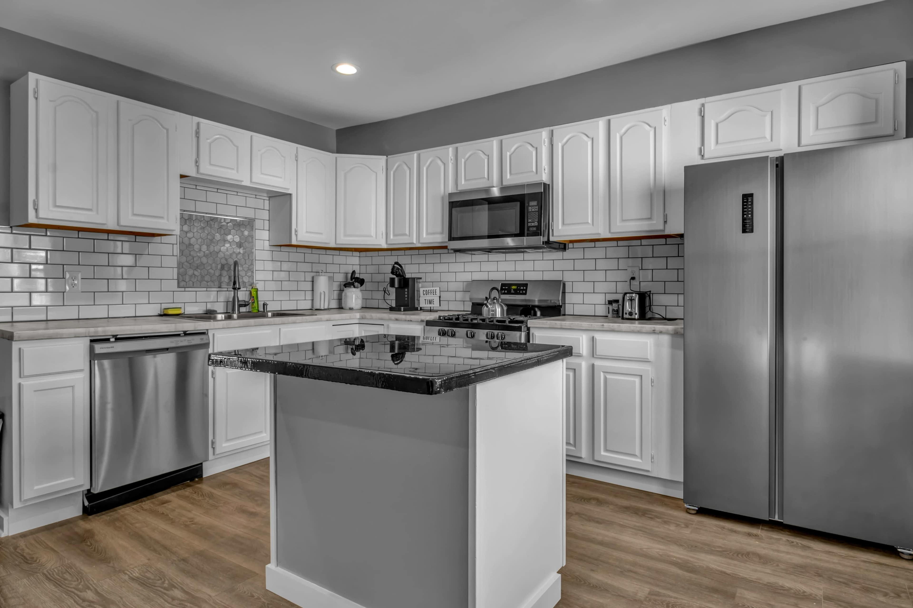 A modern kitchen with white cabinets, a stainless steel refrigerator, and a central island with a black granite countertop.