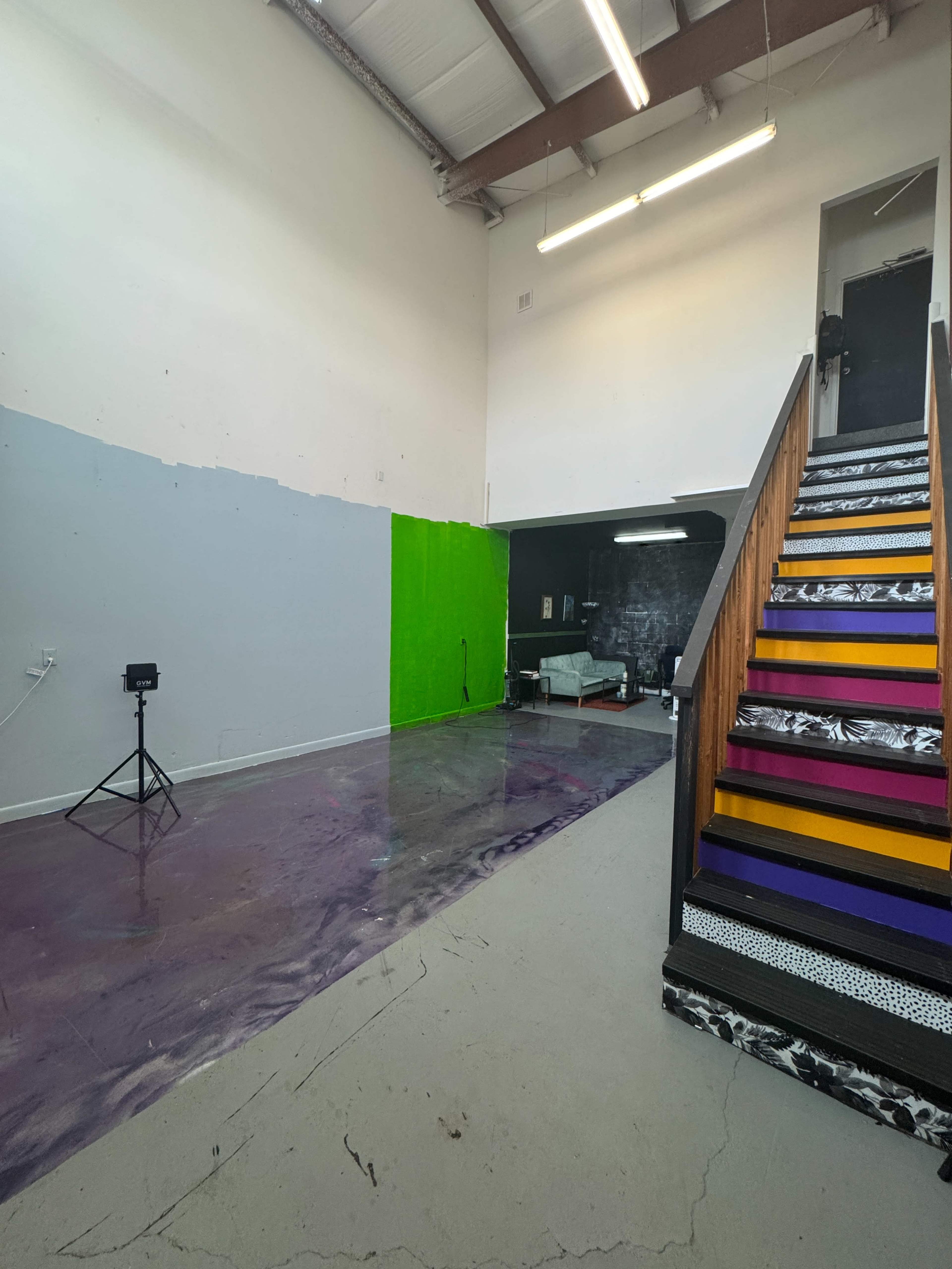 The image shows a spacious room with a staircase on the right, a purple and gray floor, and a bright green wall on the left side.