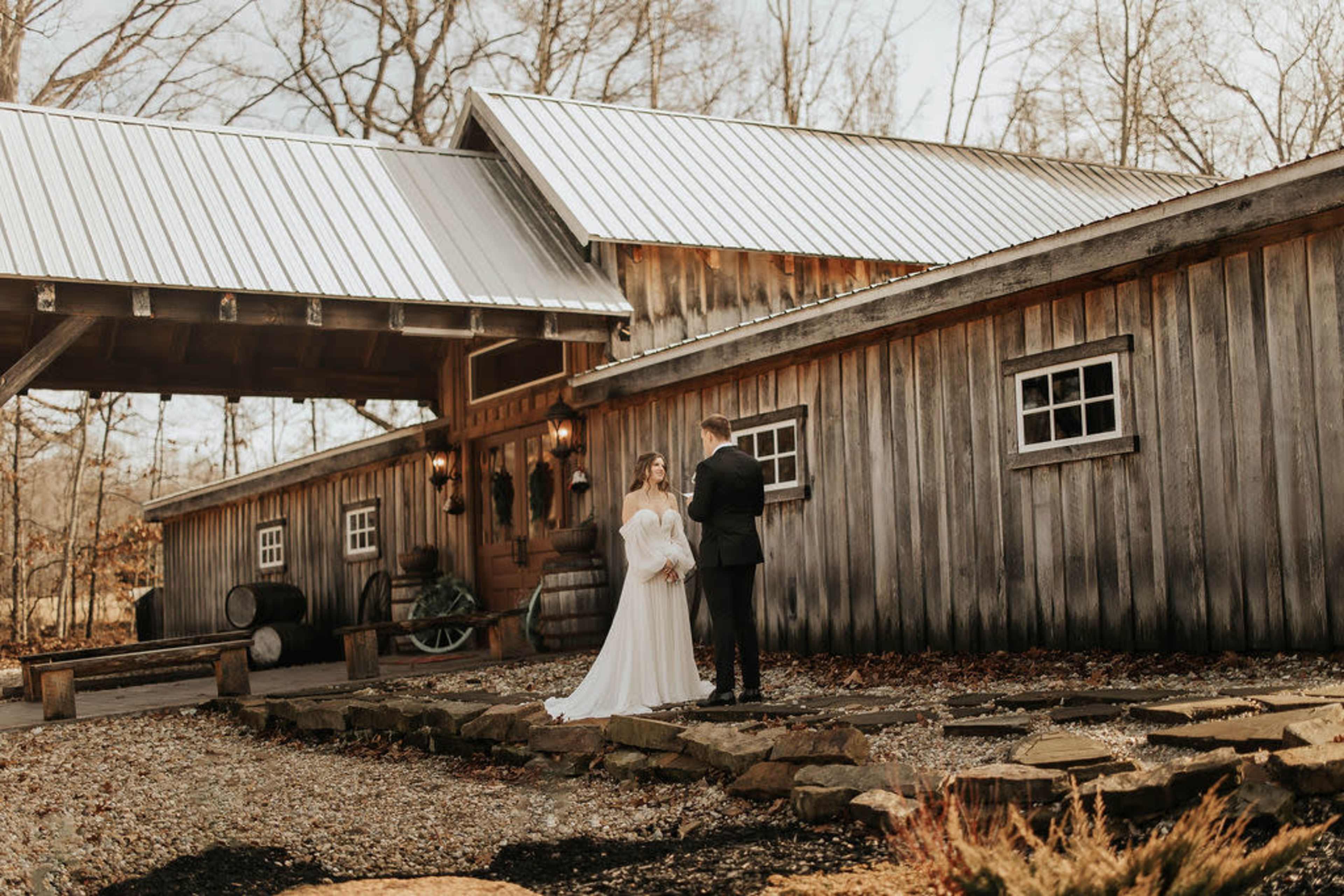 A couple stands in front of a rustic wooden building, exchanging vows while surrounded by a scenic outdoor setting.