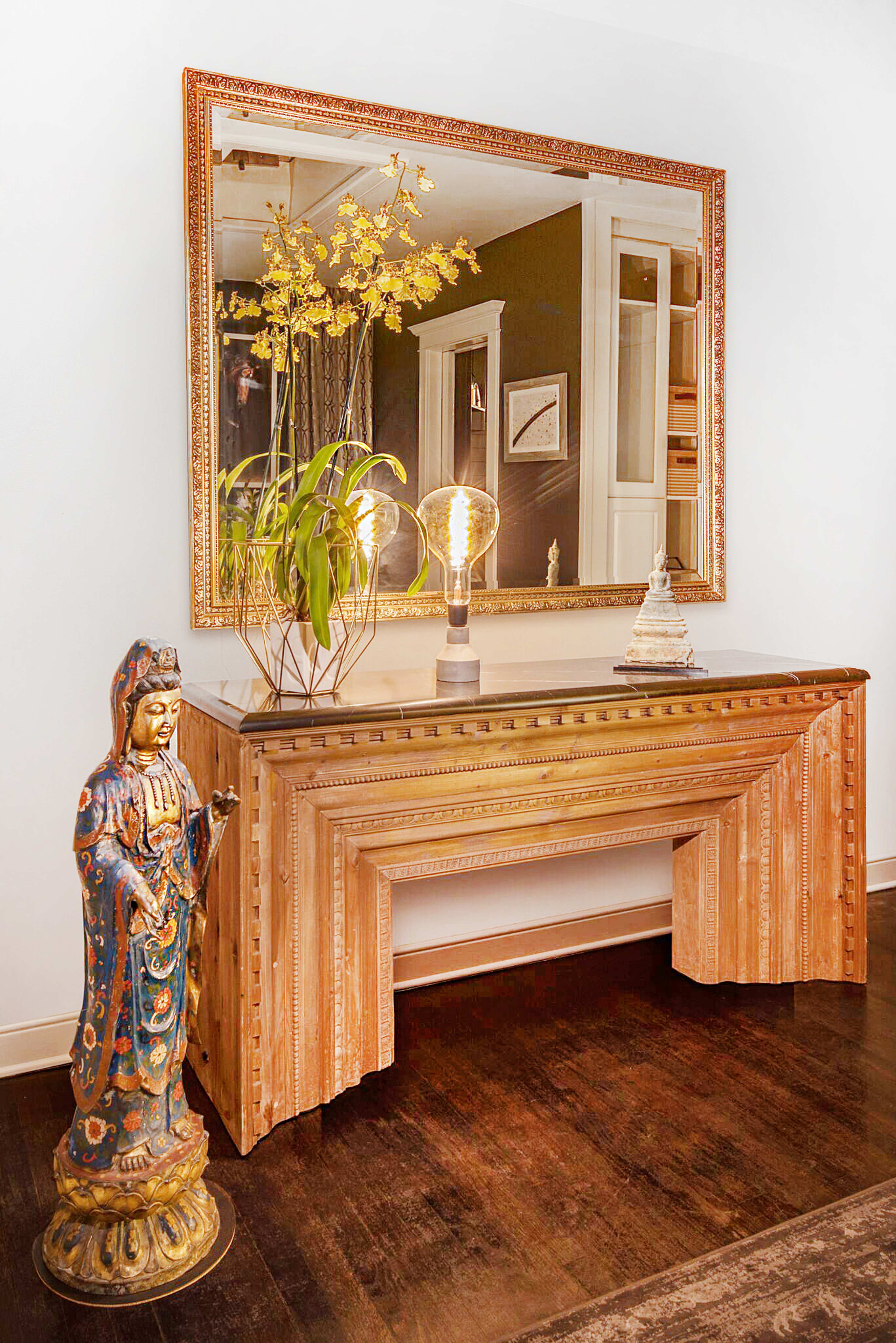 A decorative console table with a large mirror and an ornate statue stands against a wall.