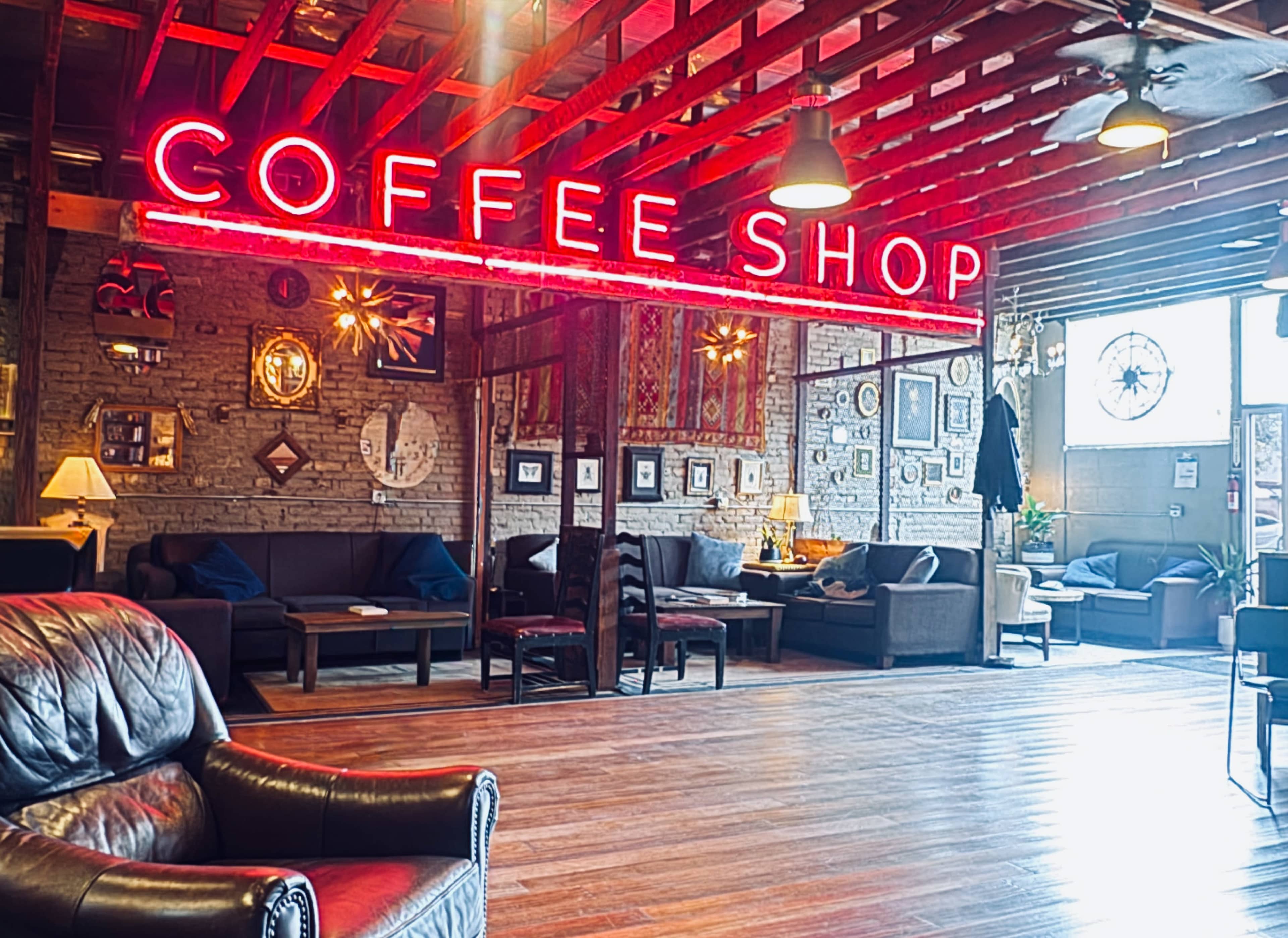 The image shows a cozy coffee shop interior with a prominent neon sign reading "COFFEE SHOP" and wooden beams overhead.