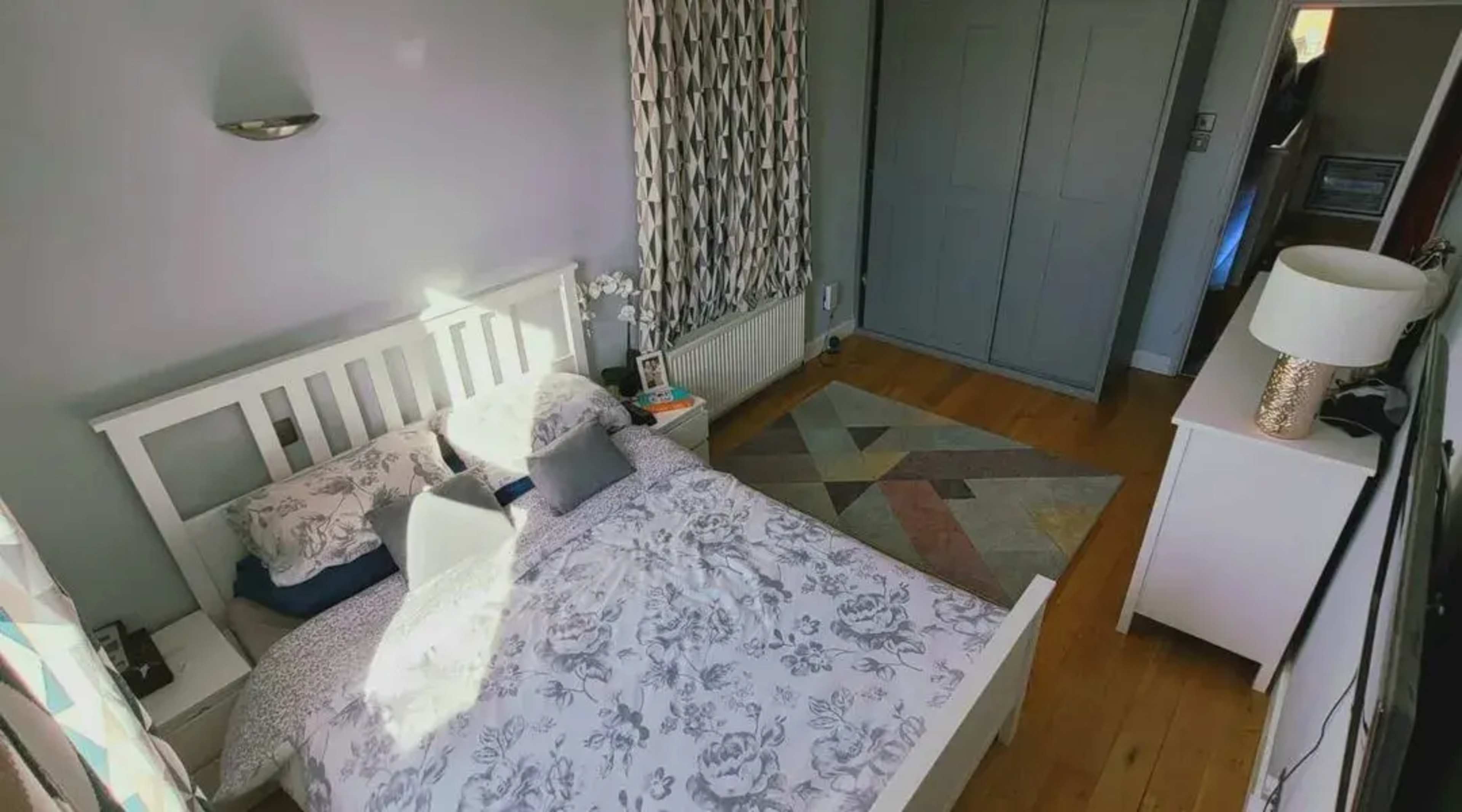 A neatly arranged bedroom featuring a white bed with patterned bedding, a light wooden floor, and a geometric rug.