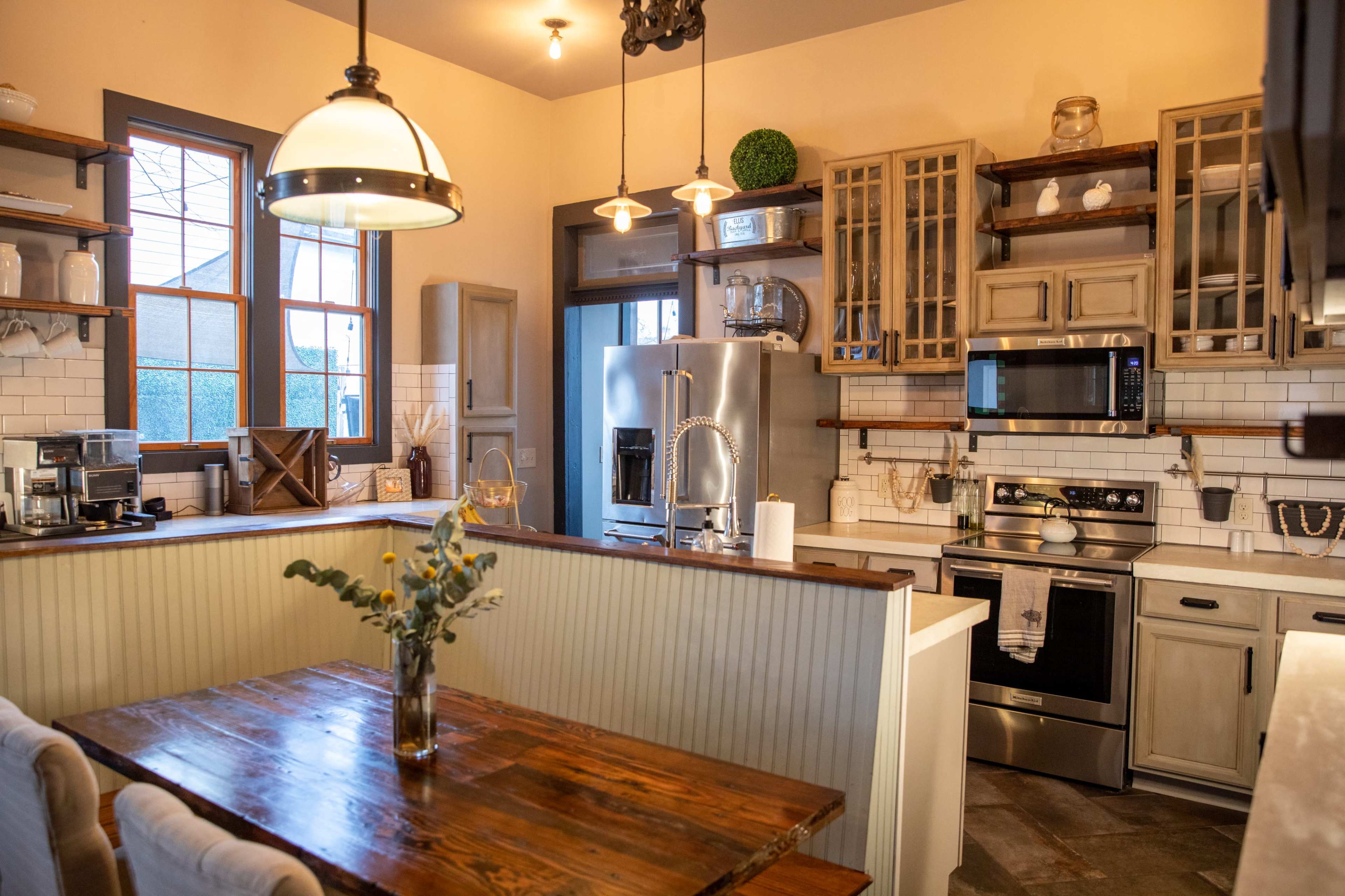 A kitchen featuring wooden shelves, a stainless steel refrigerator, an oven, and a dining table with flowers in a vase.