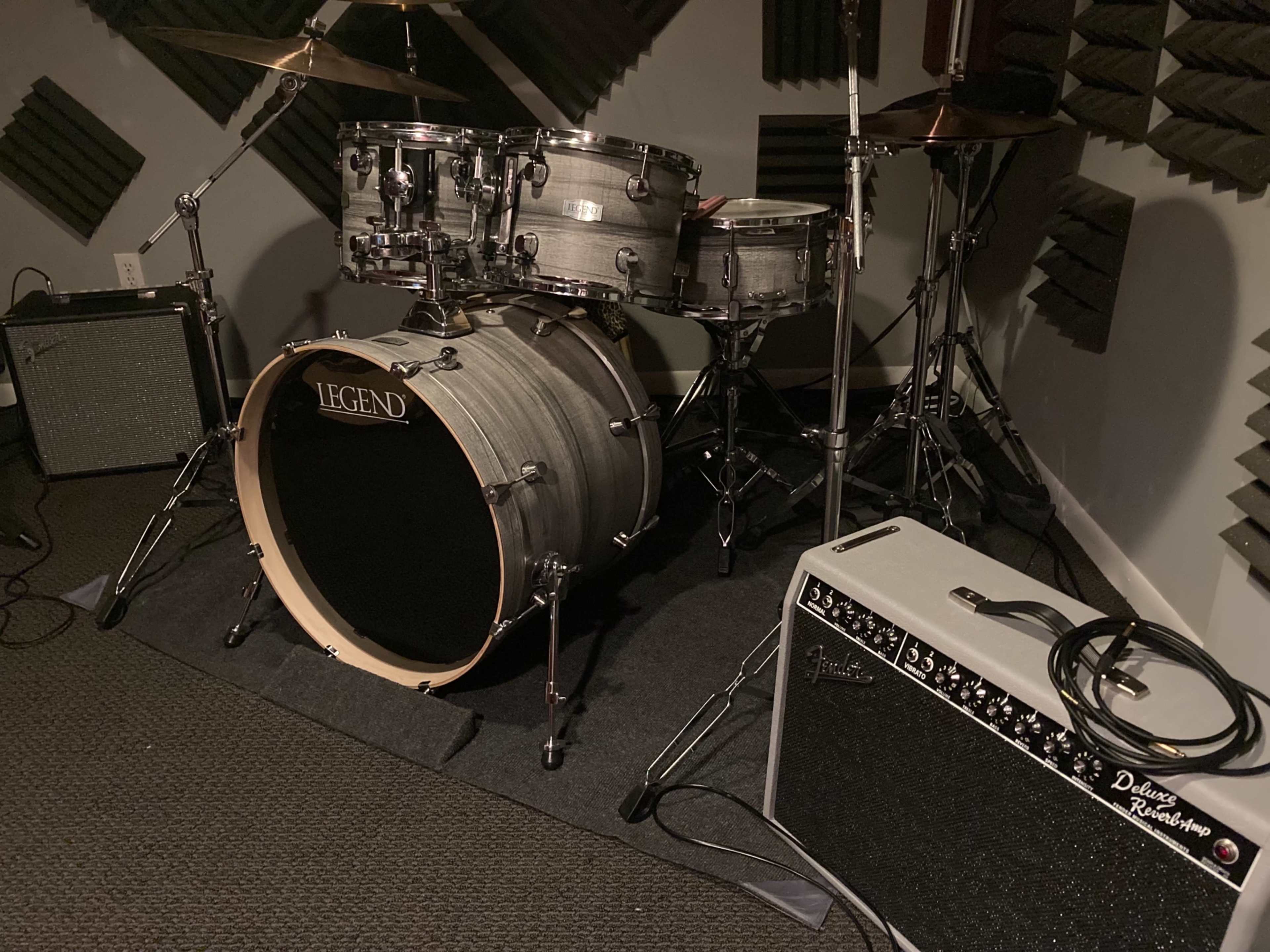 A gray drum set with a bass drum and snare is positioned beside an amplifier in a soundproof studio.