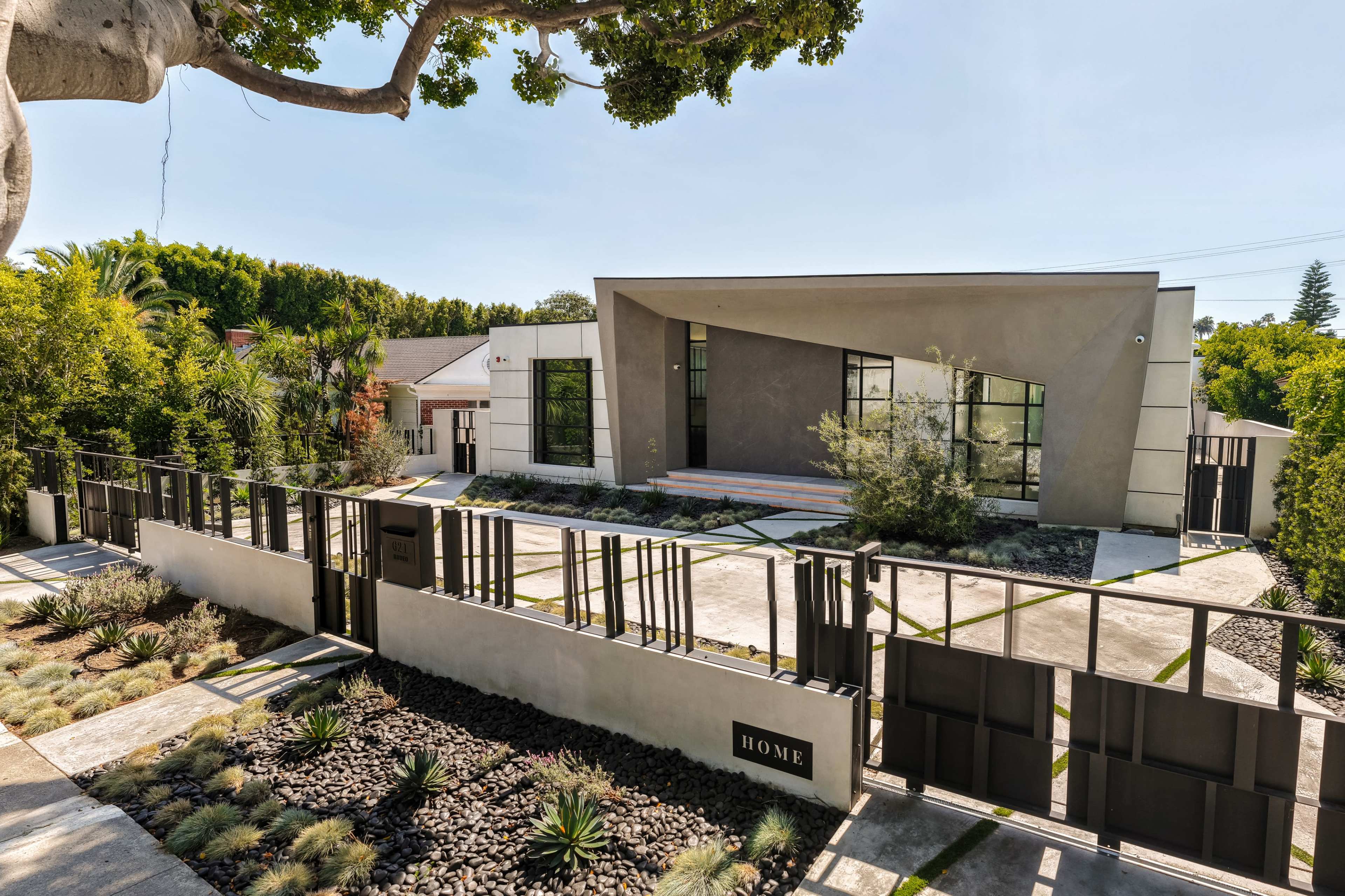 The image shows a modern house with a landscaped front yard, featuring a linear fence and a driveway leading to the entrance.