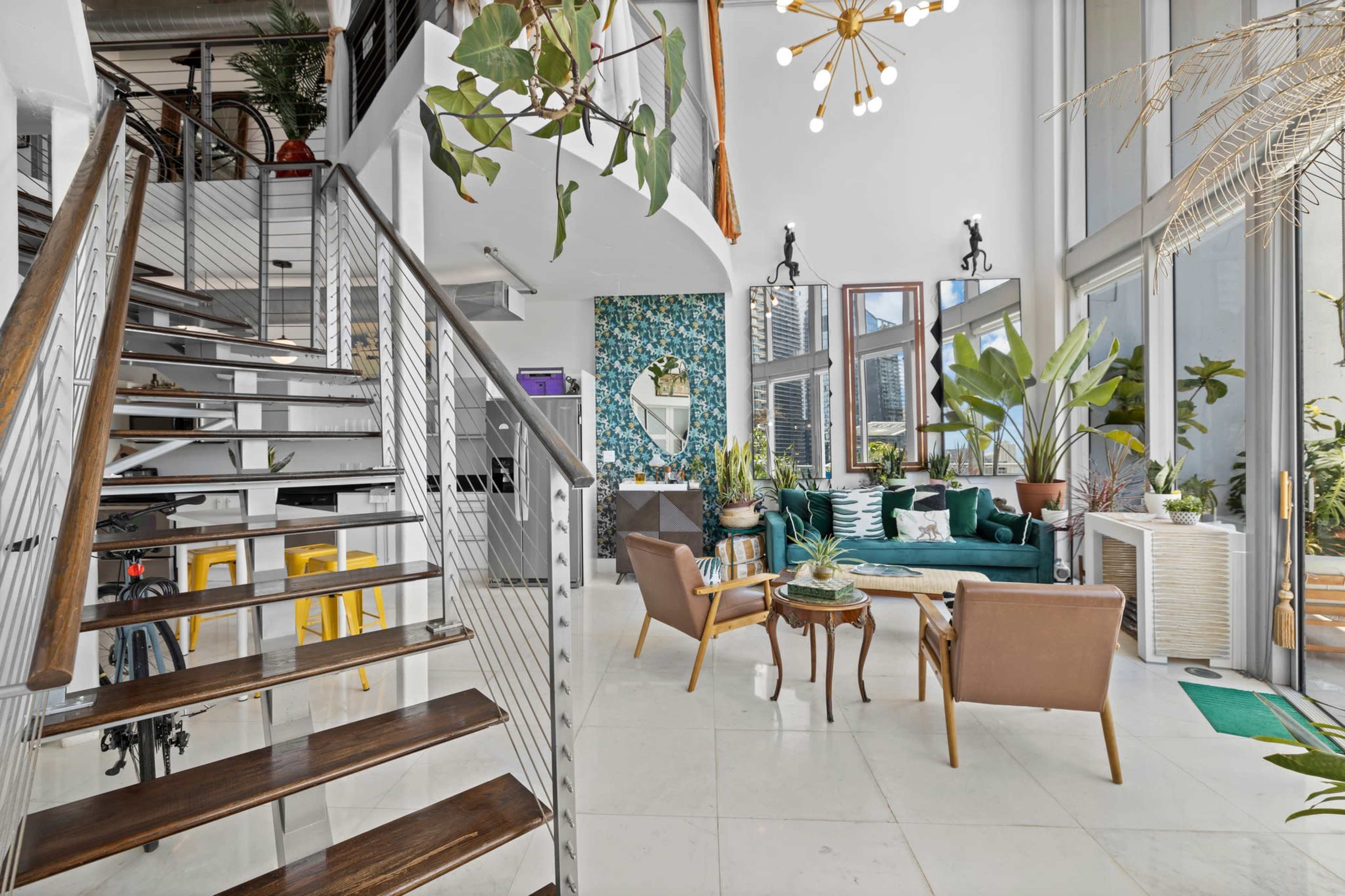 A modern interior space featuring a staircase, a seating area with plants, large windows, and decorative elements on the walls.