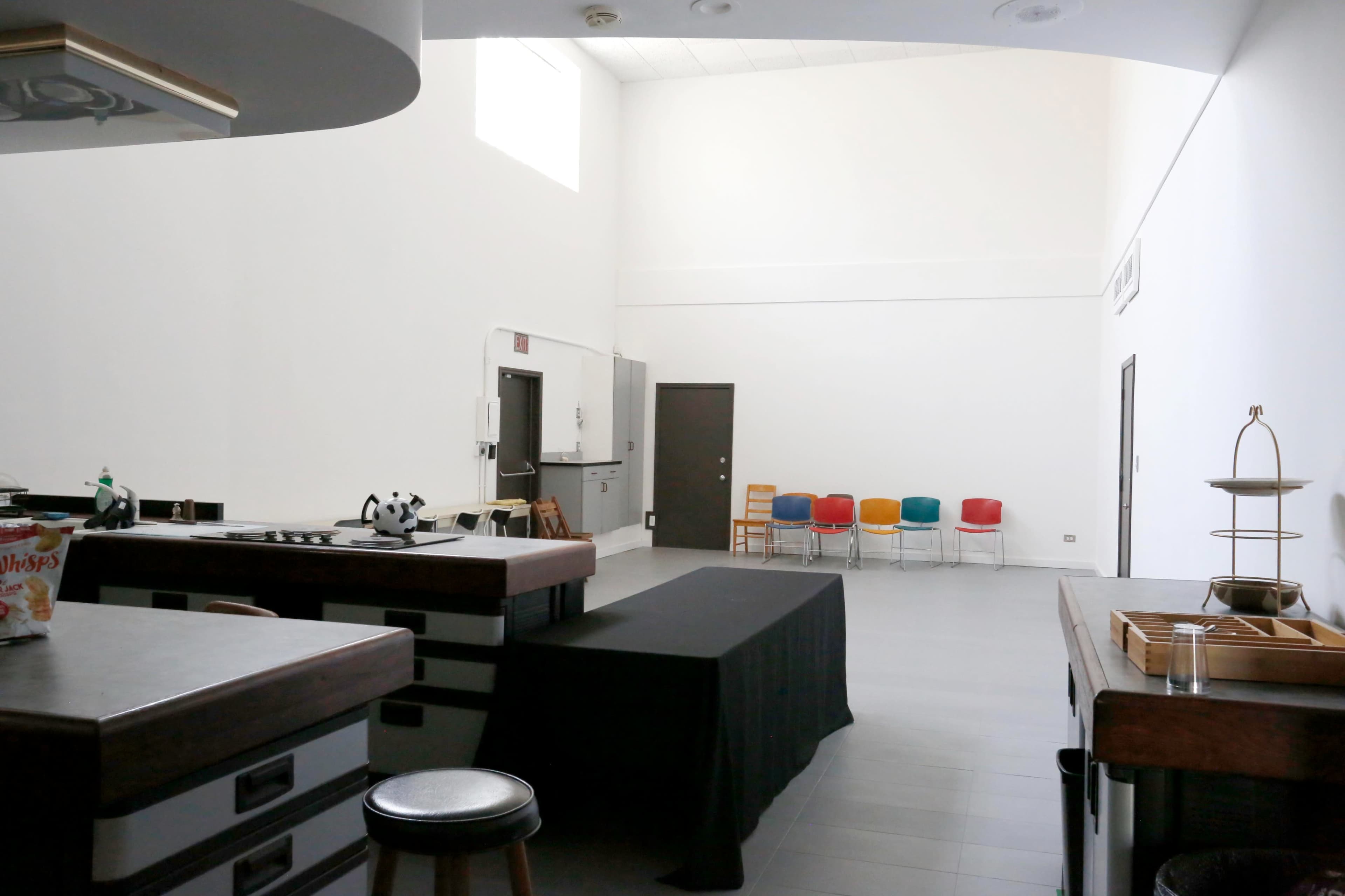 A spacious kitchen area with a large black table and colorful chairs lined up against the wall.
