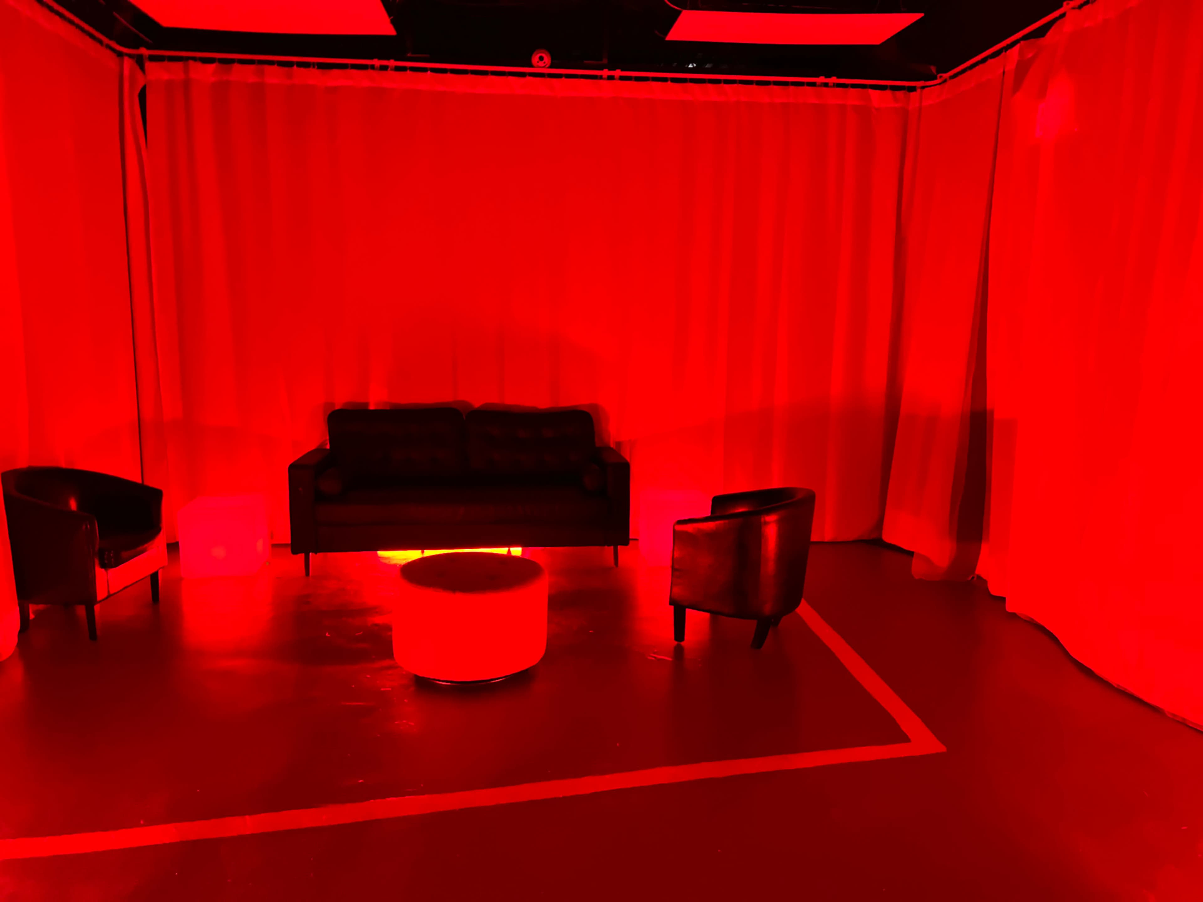 The scene features a room with red curtains, a black sofa, two black chairs, and a circular table, all illuminated by red lighting.