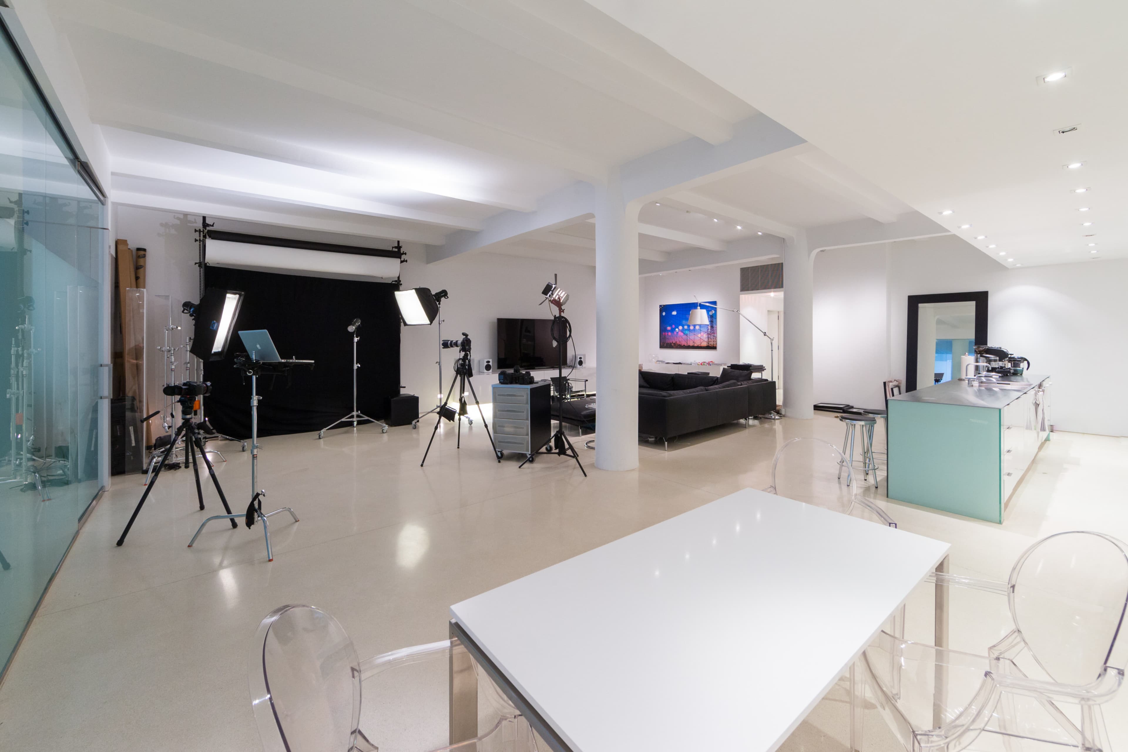 The image shows a modern studio space equipped with filming equipment, a seating area, and a kitchen counter.