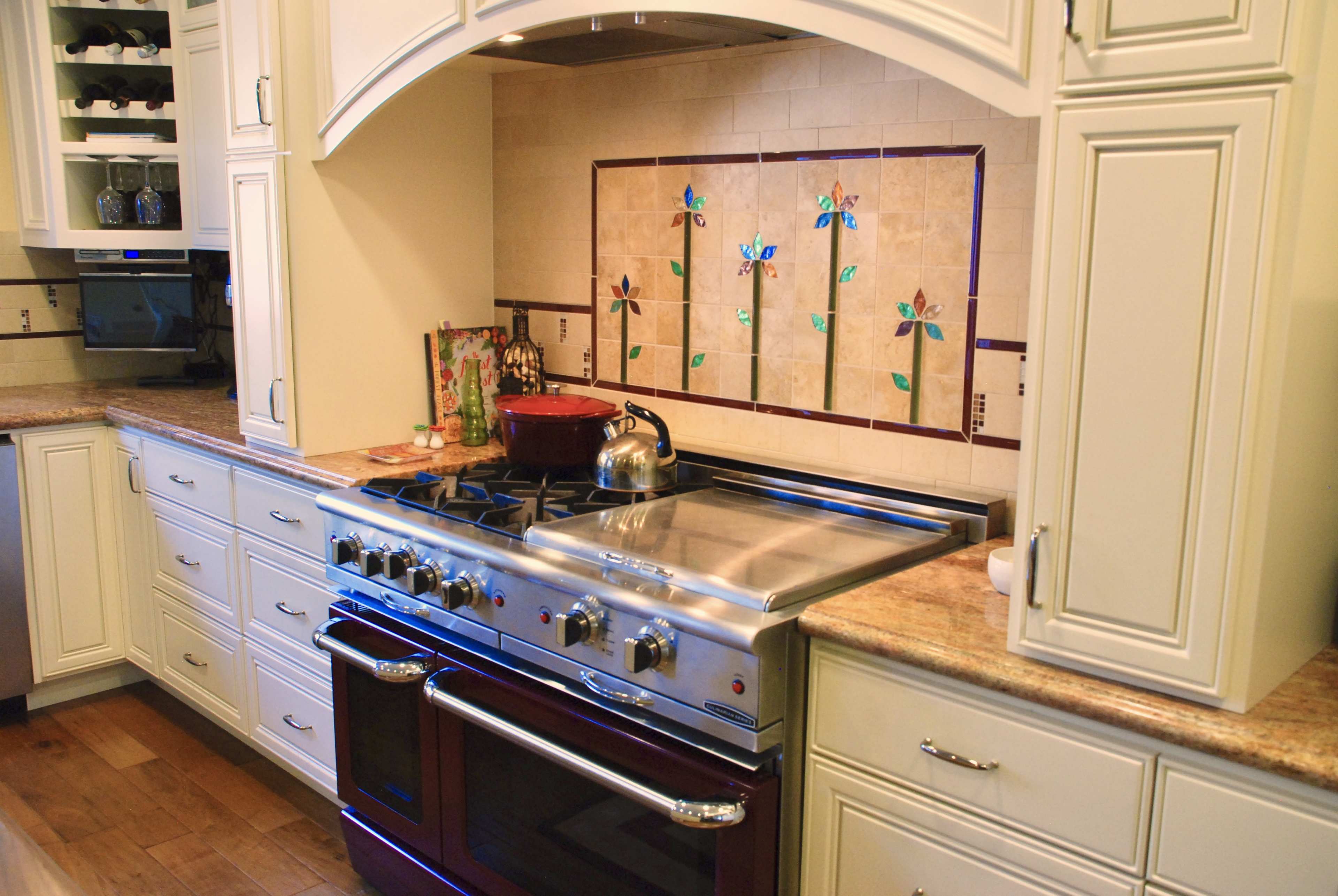 A modern kitchen featuring a stainless steel stove with a decorative tile backsplash and a kettle on the stovetop.