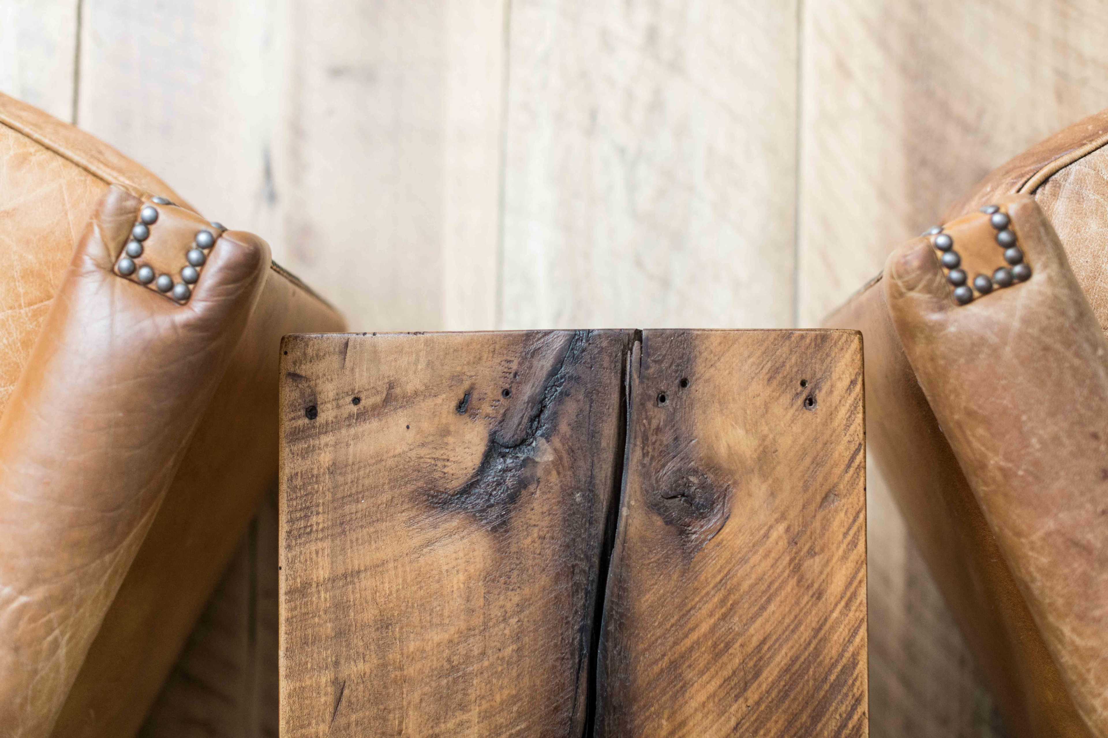 A close-up view of two leather chair arms positioned beside a wooden table with a visible natural grain.