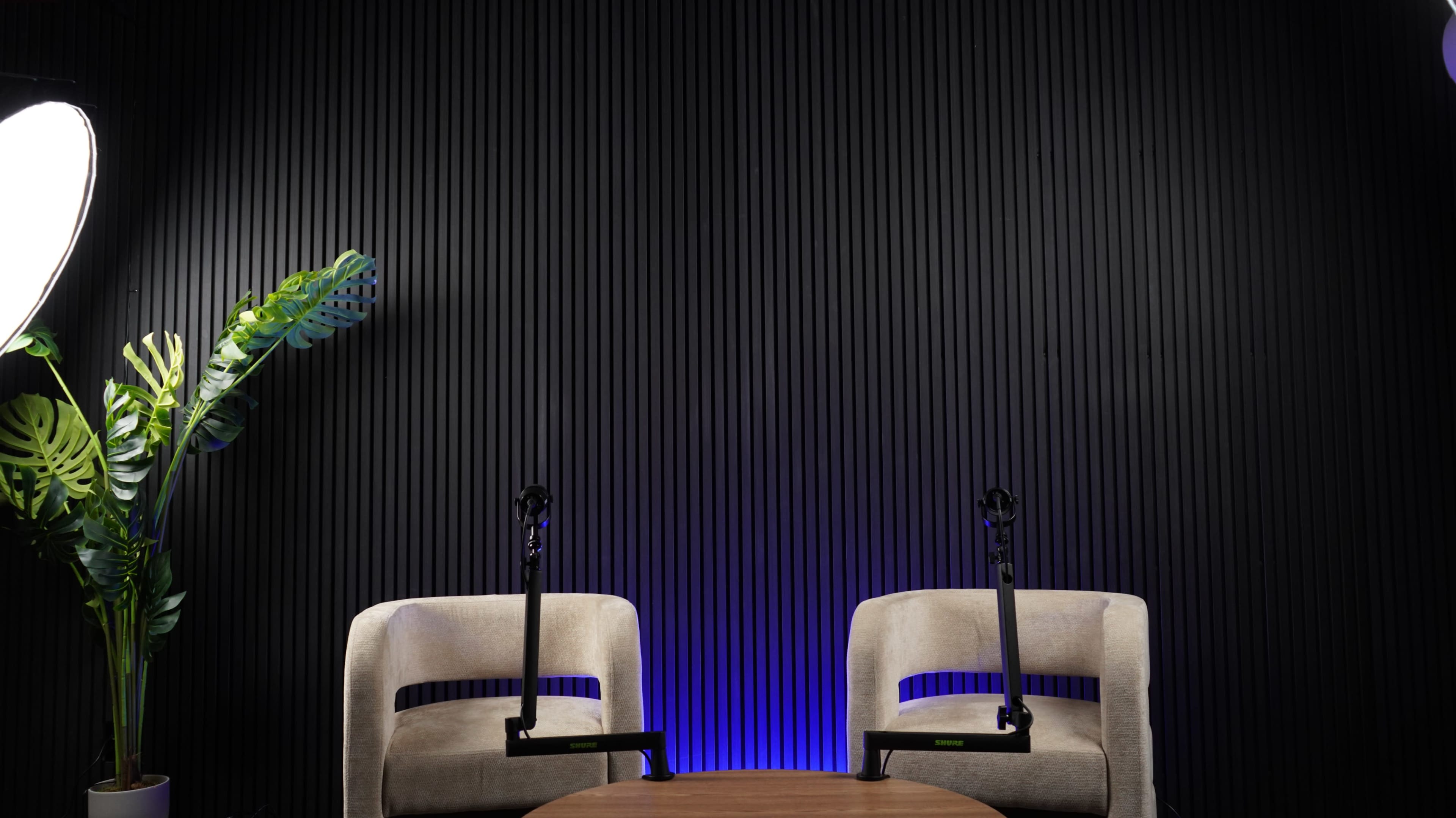 The scene features two empty chairs with microphone stands and a small round table in front of a textured black wall, illuminated by soft blue lighting.