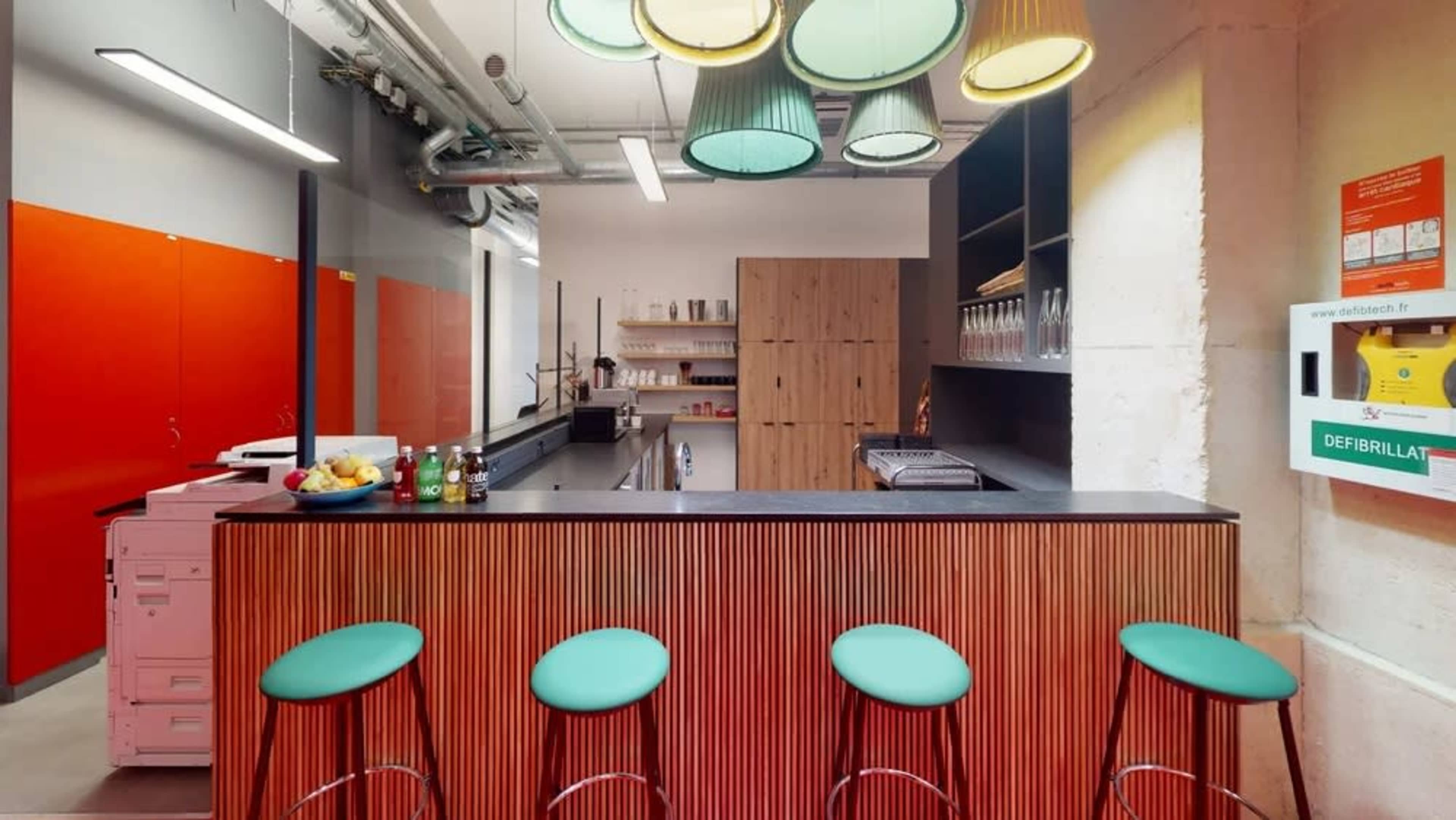 A modern kitchen with a bar area featuring four turquoise stools, wooden cabinetry, and colorful pendant lights hanging above.