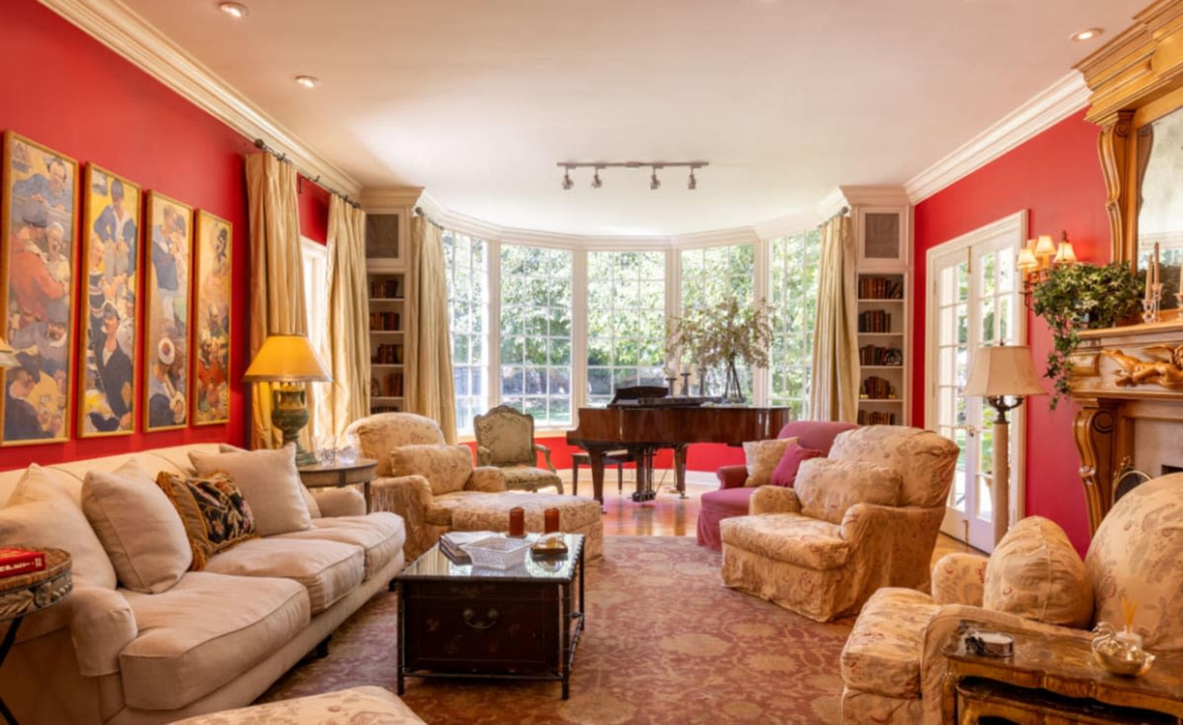 A cozy living room with red walls, a grand piano, and several comfortable seating arrangements around a coffee table.