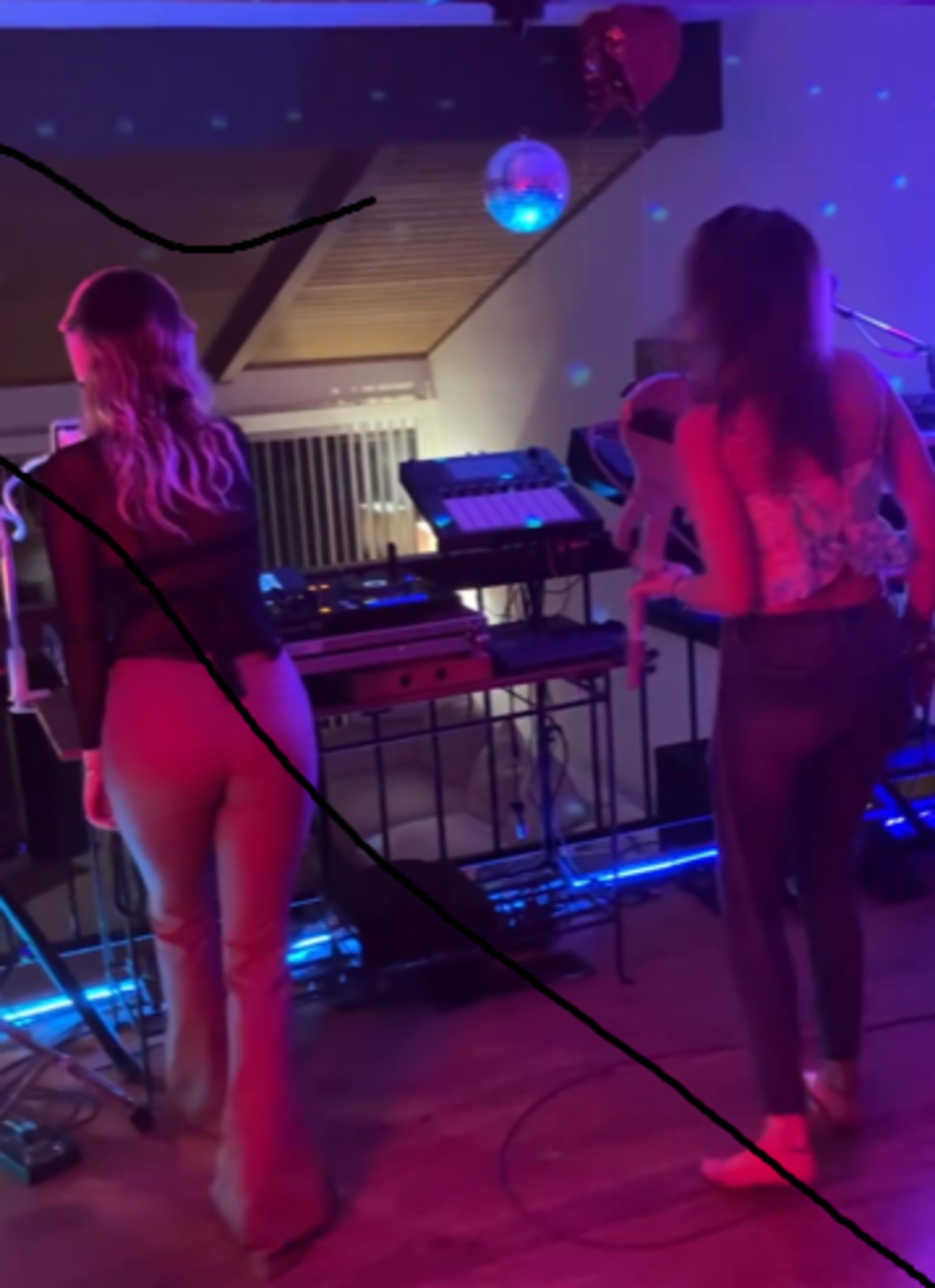 Two women perform on stage with musical equipment and colorful lights in the background.