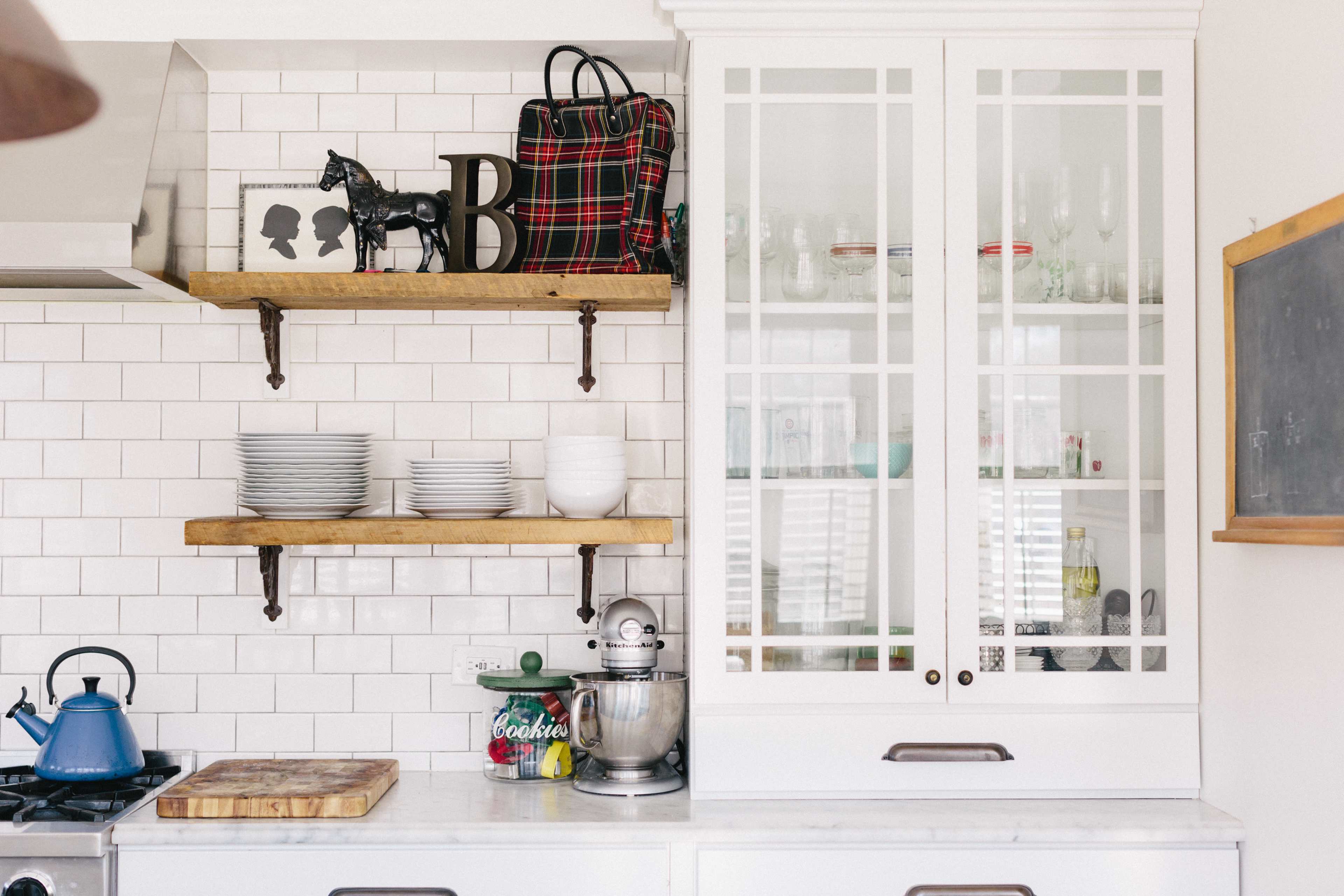 The kitchen features white cabinetry with glass doors, open wooden shelves holding plates and a decorative horse, and a blue kettle on the stovetop.