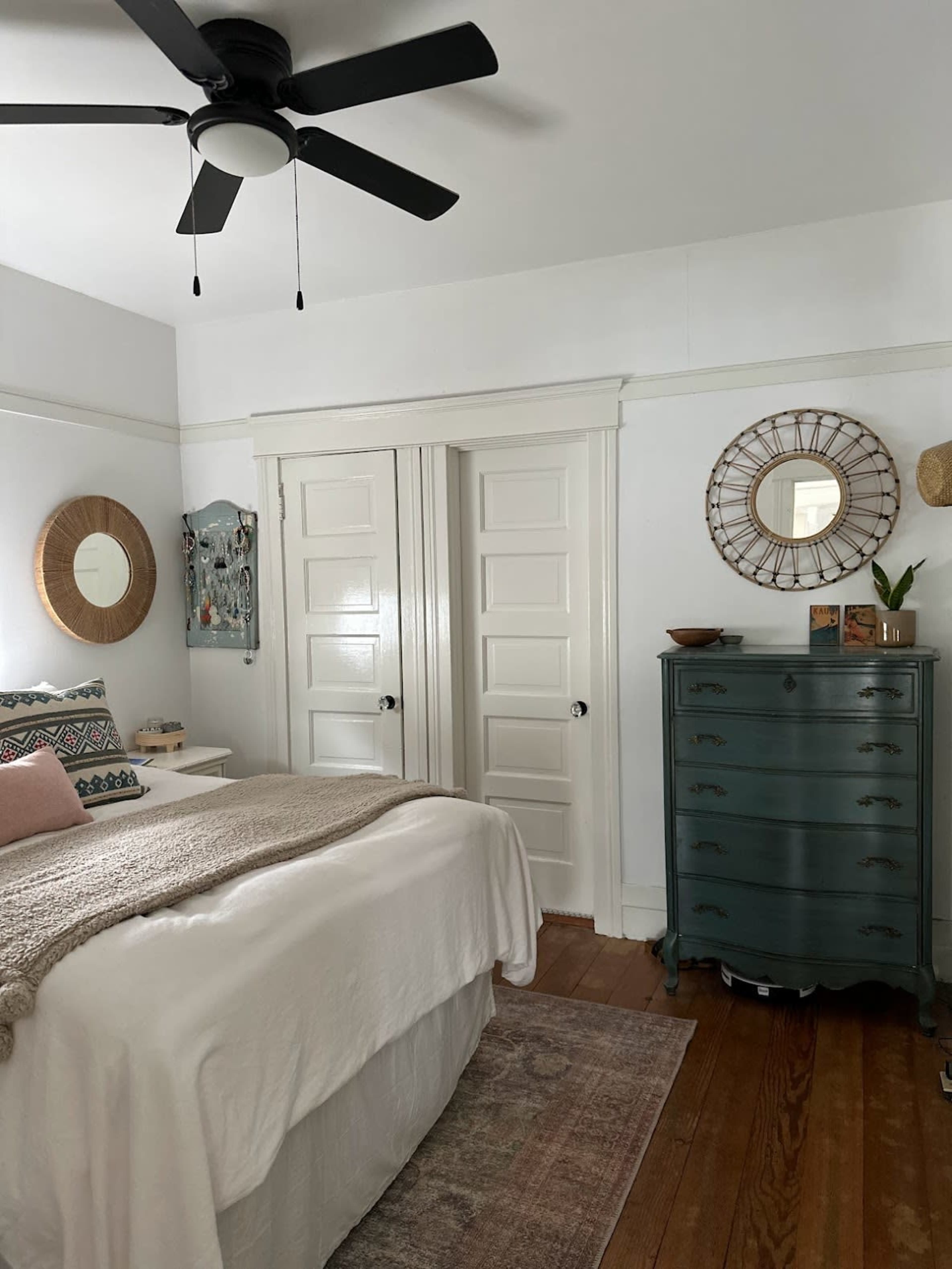 A cozy bedroom featuring a bed with a light coverlet, a green dresser, and two closed white doors.