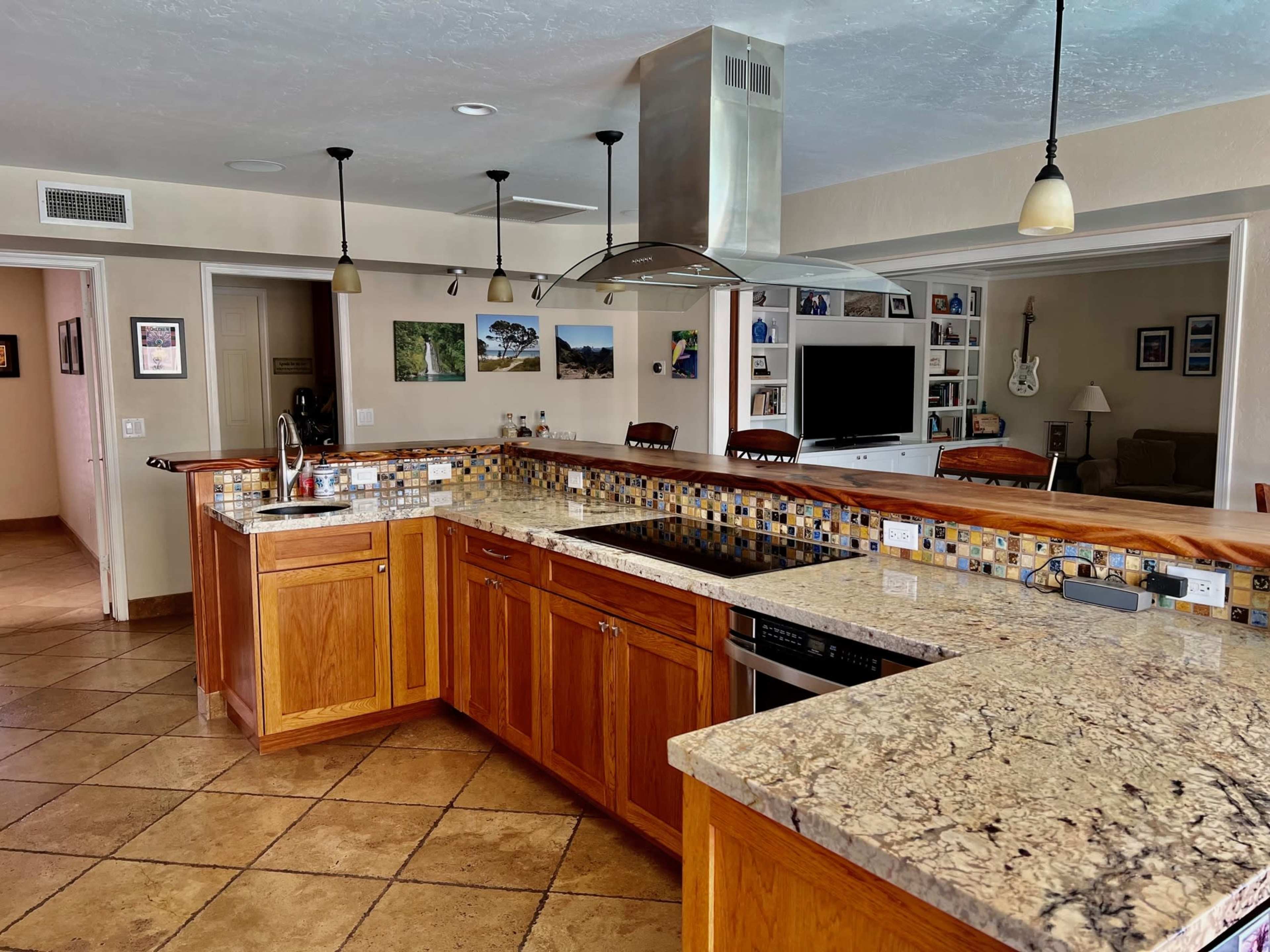 A spacious kitchen with wooden cabinets, a large granite countertop, and an island equipped with a stove and an overhead vent.