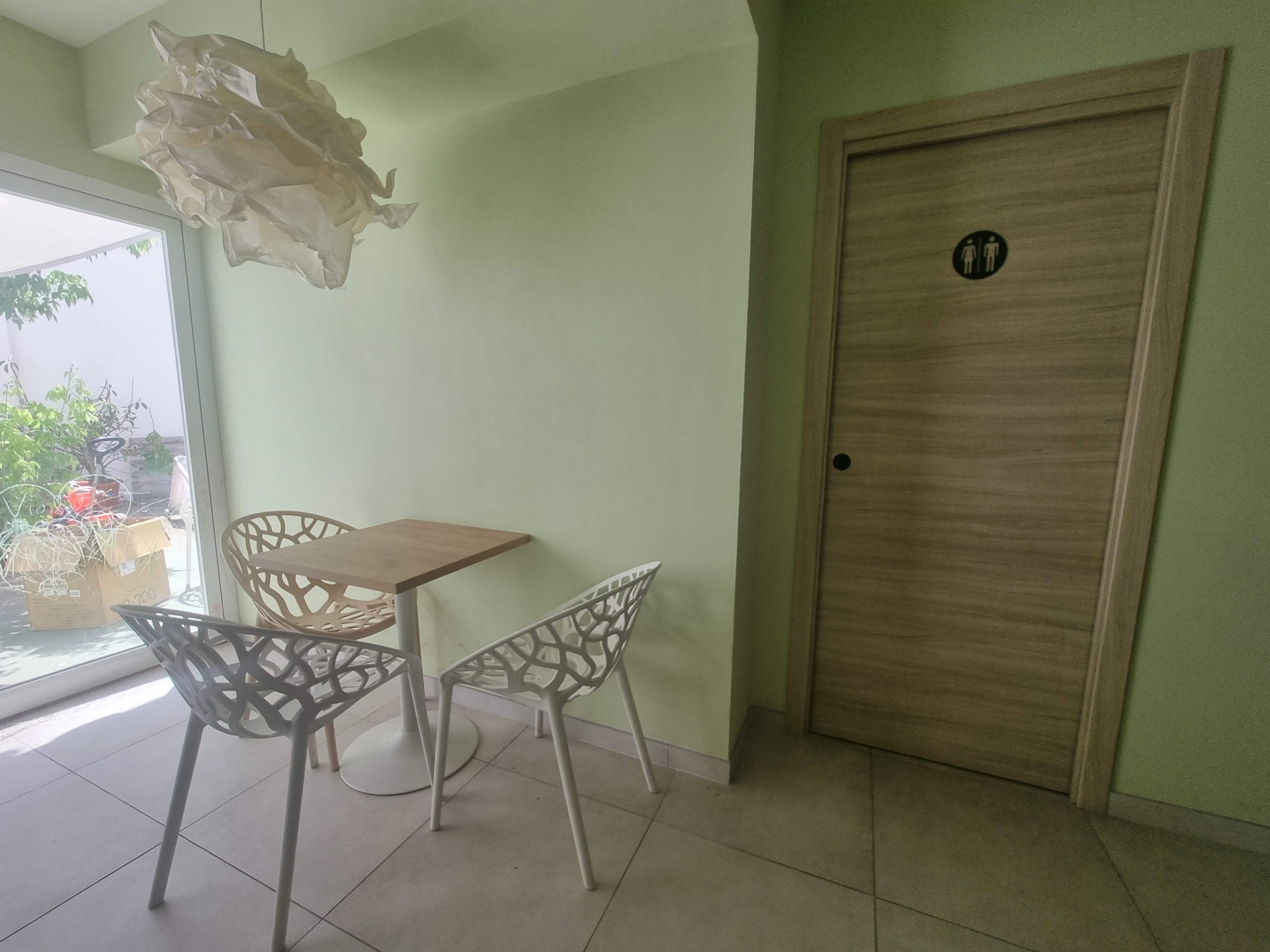 The image shows a small dining area with two white chairs and a wooden table next to a door labeled as a restroom.