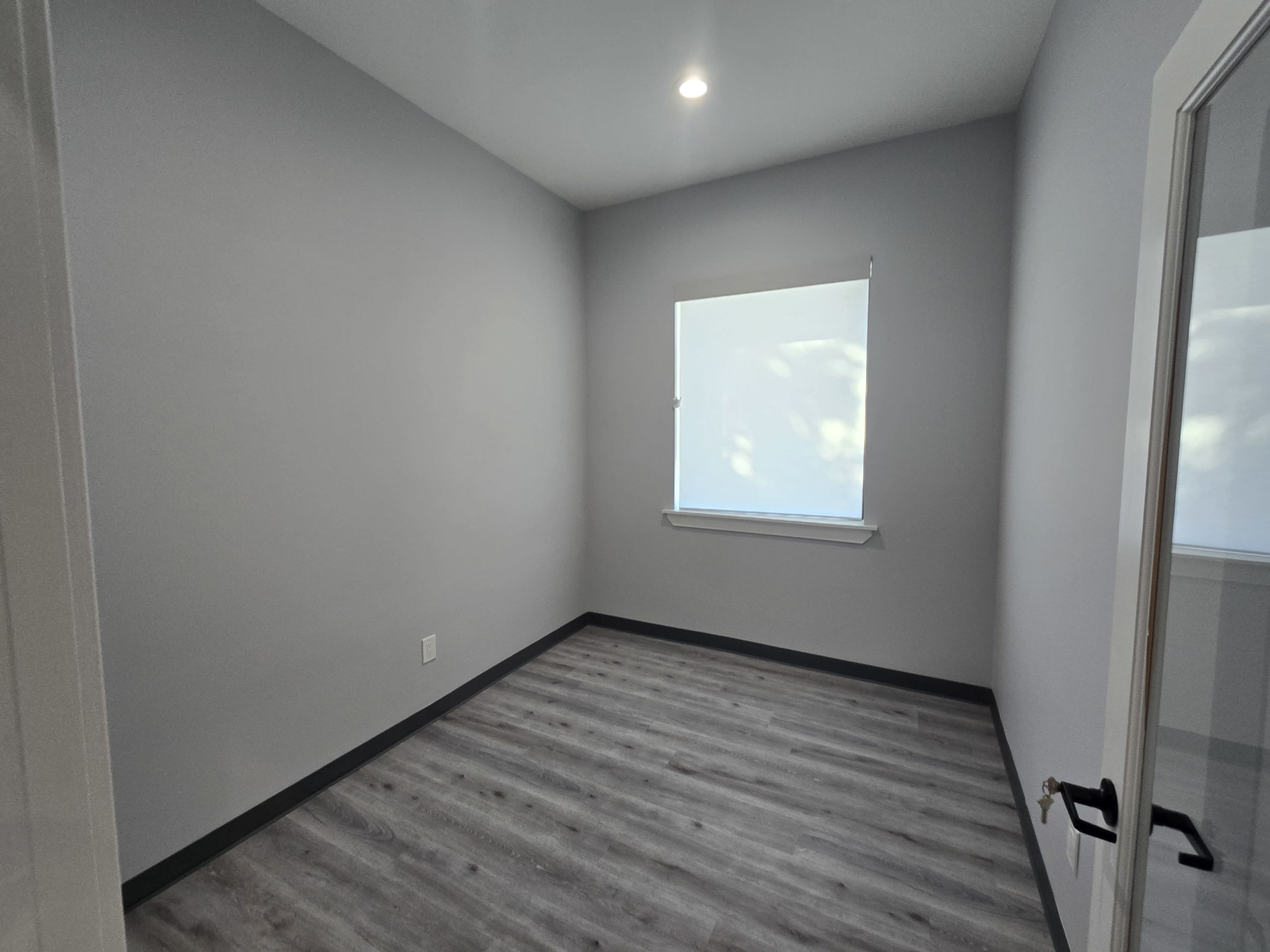 The image shows an empty room with gray walls, a single window, and a light-colored wooden floor.