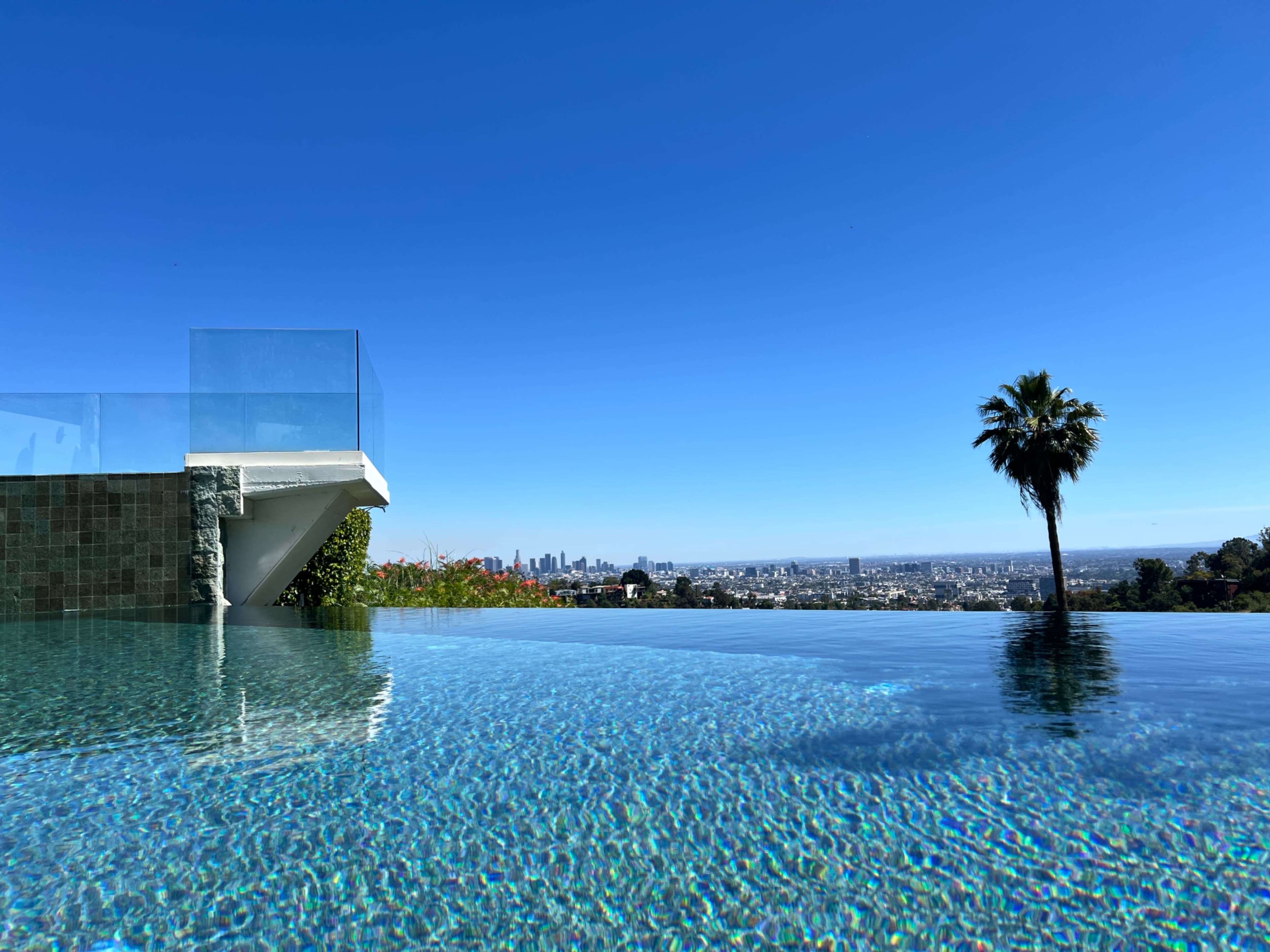 A luxurious infinity pool reflects the clear blue sky and offers a panoramic view of the city skyline.