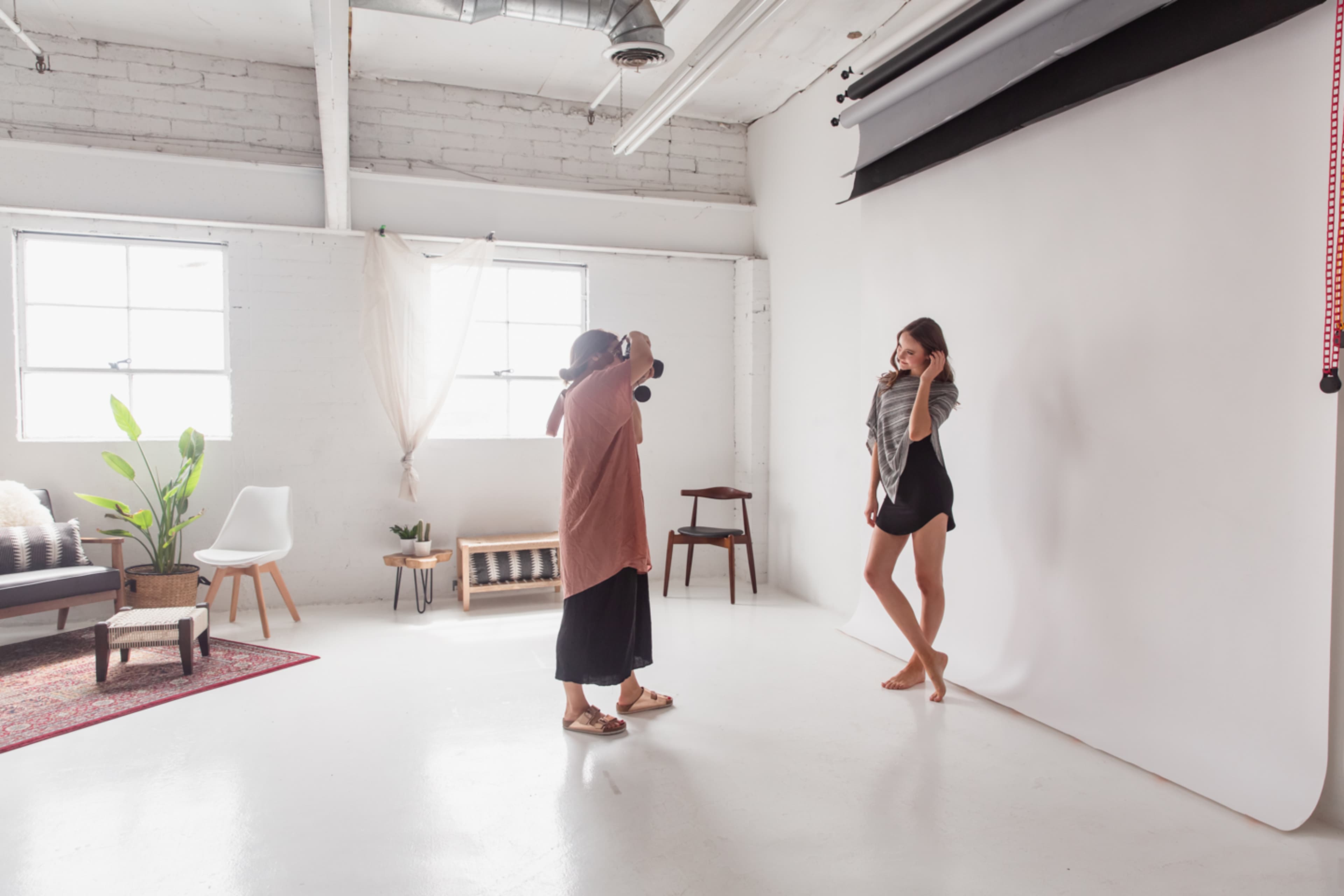 A photographer captures a model posing in a studio with bright lighting and a plain backdrop.