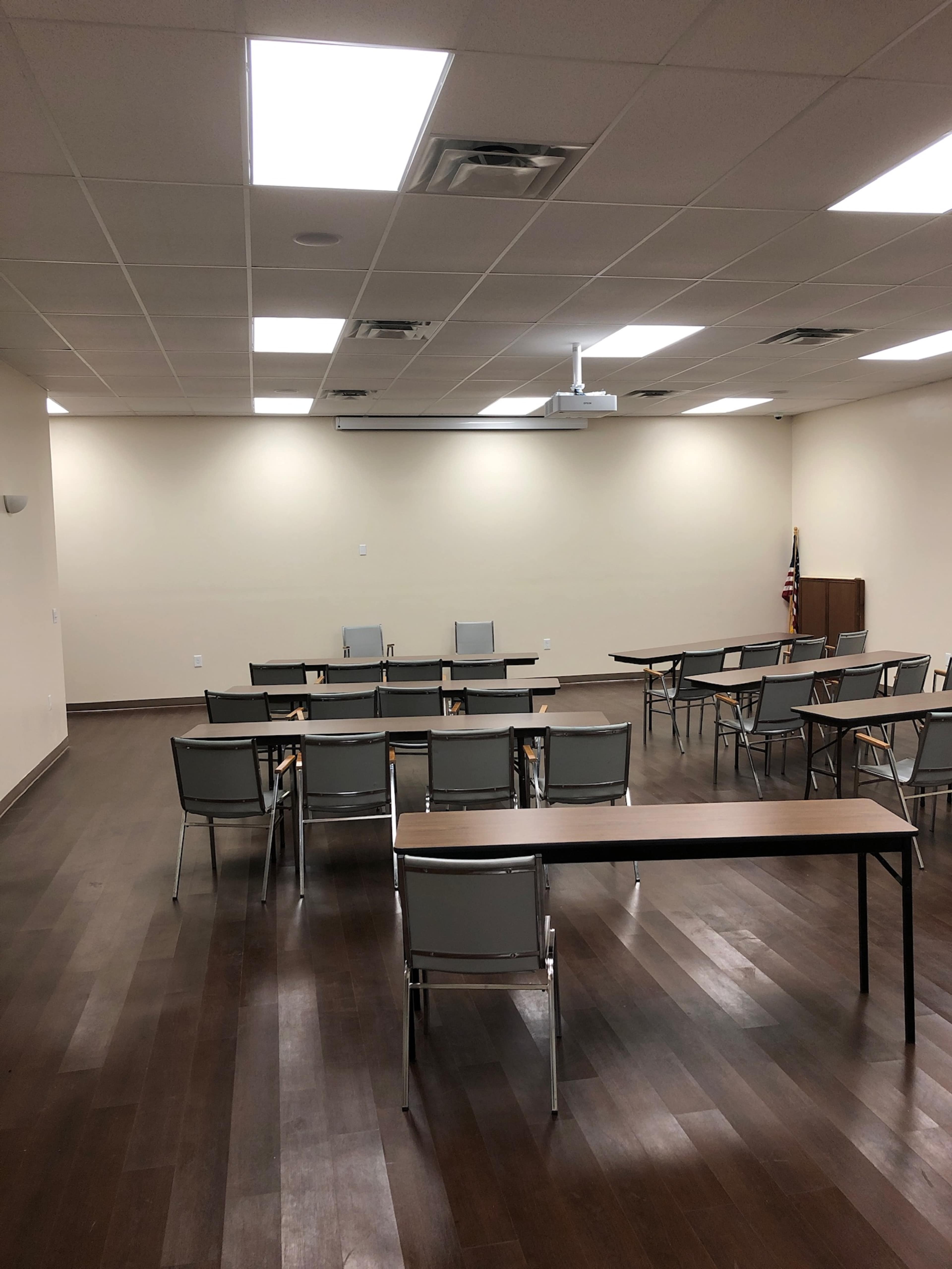 A meeting room with rows of chairs and tables arranged in a semi-circle, illuminated by overhead lights.
