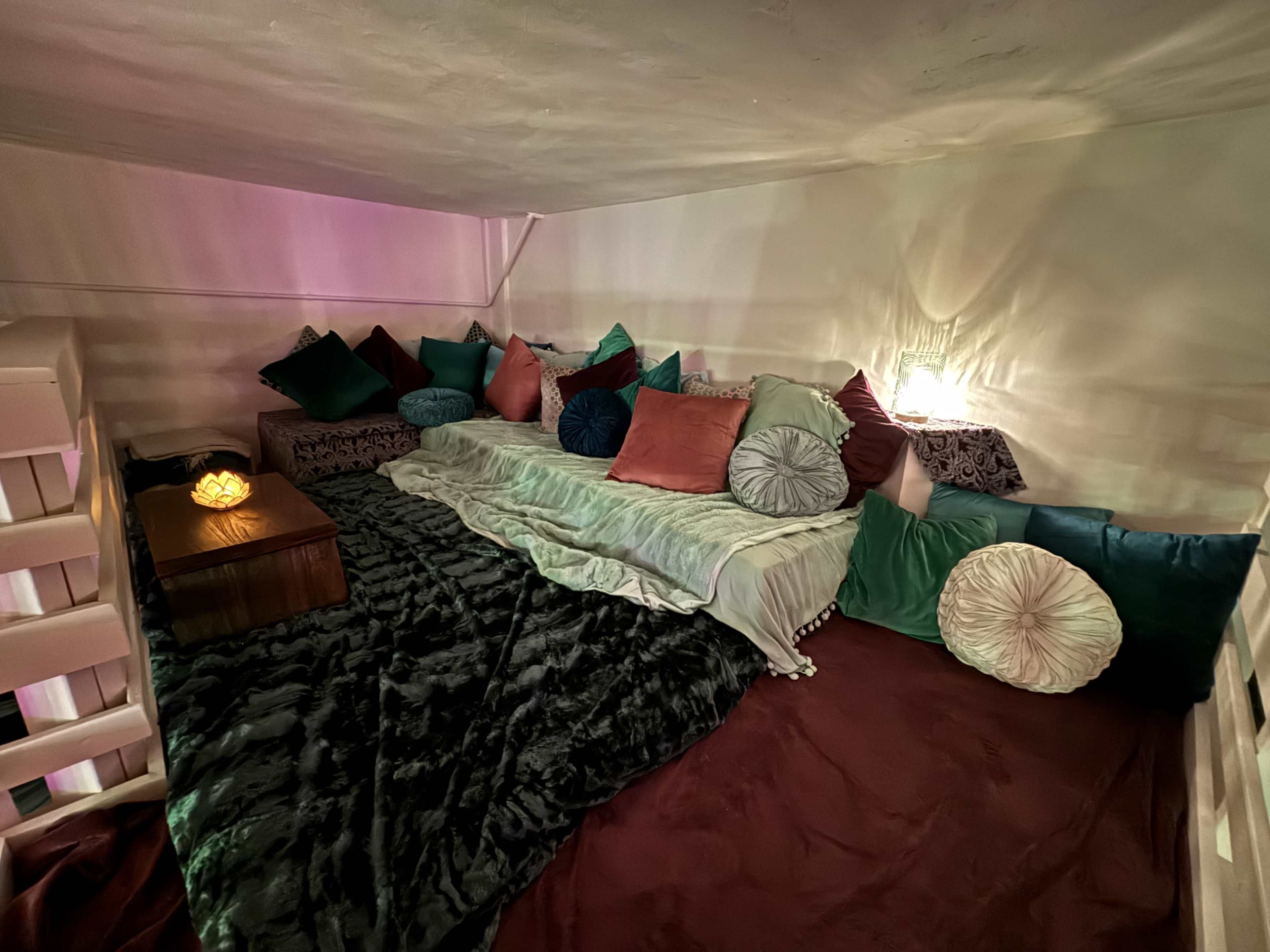 A cozy interior space with a low wooden table surrounded by various cushions and blankets.