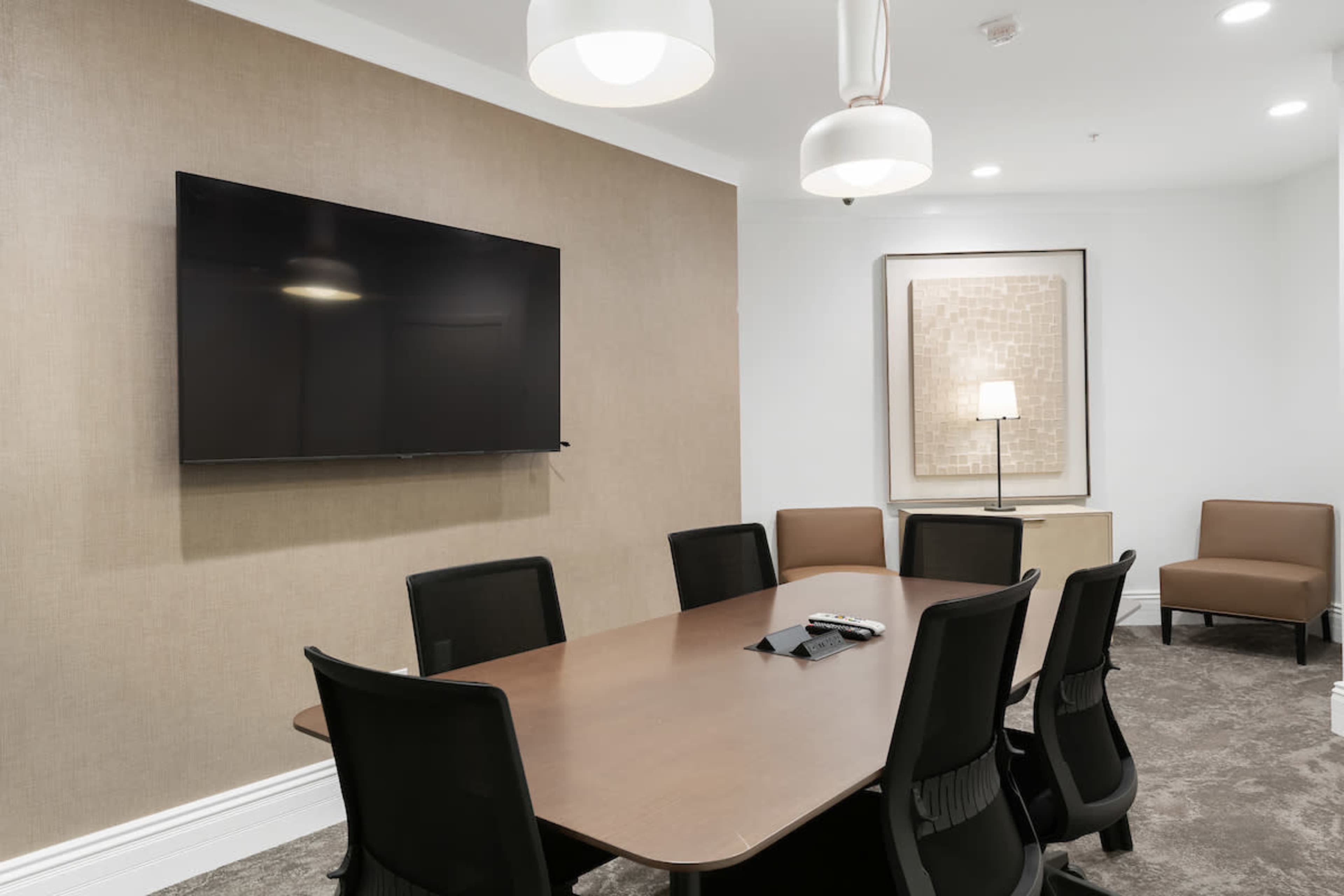 A modern meeting room with a large table, eight black chairs, a wall-mounted television, and a decorative piece on the wall.