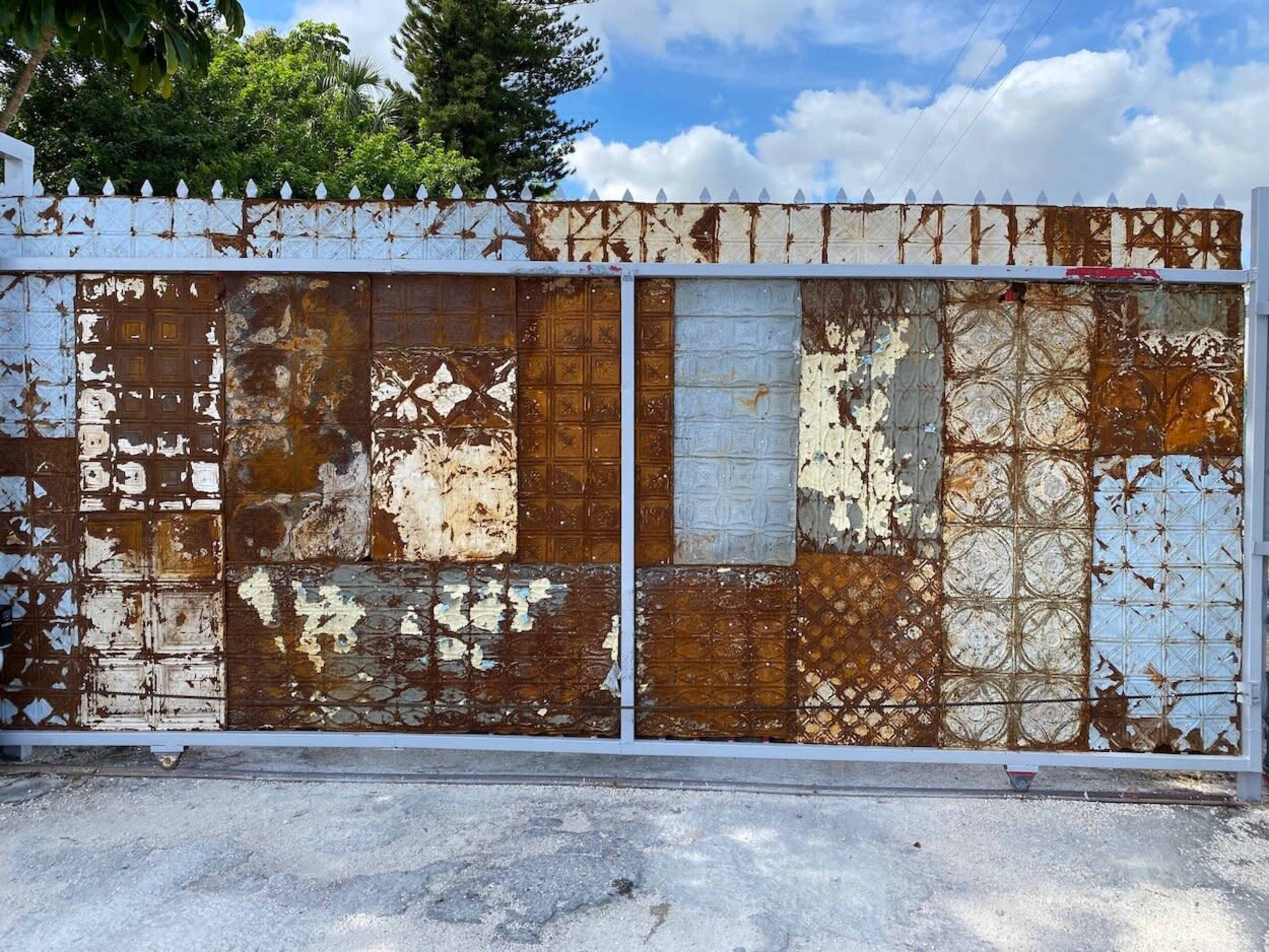 A metal gate covered with a patchwork of rusted and peeling painted panels in various textures and colors.