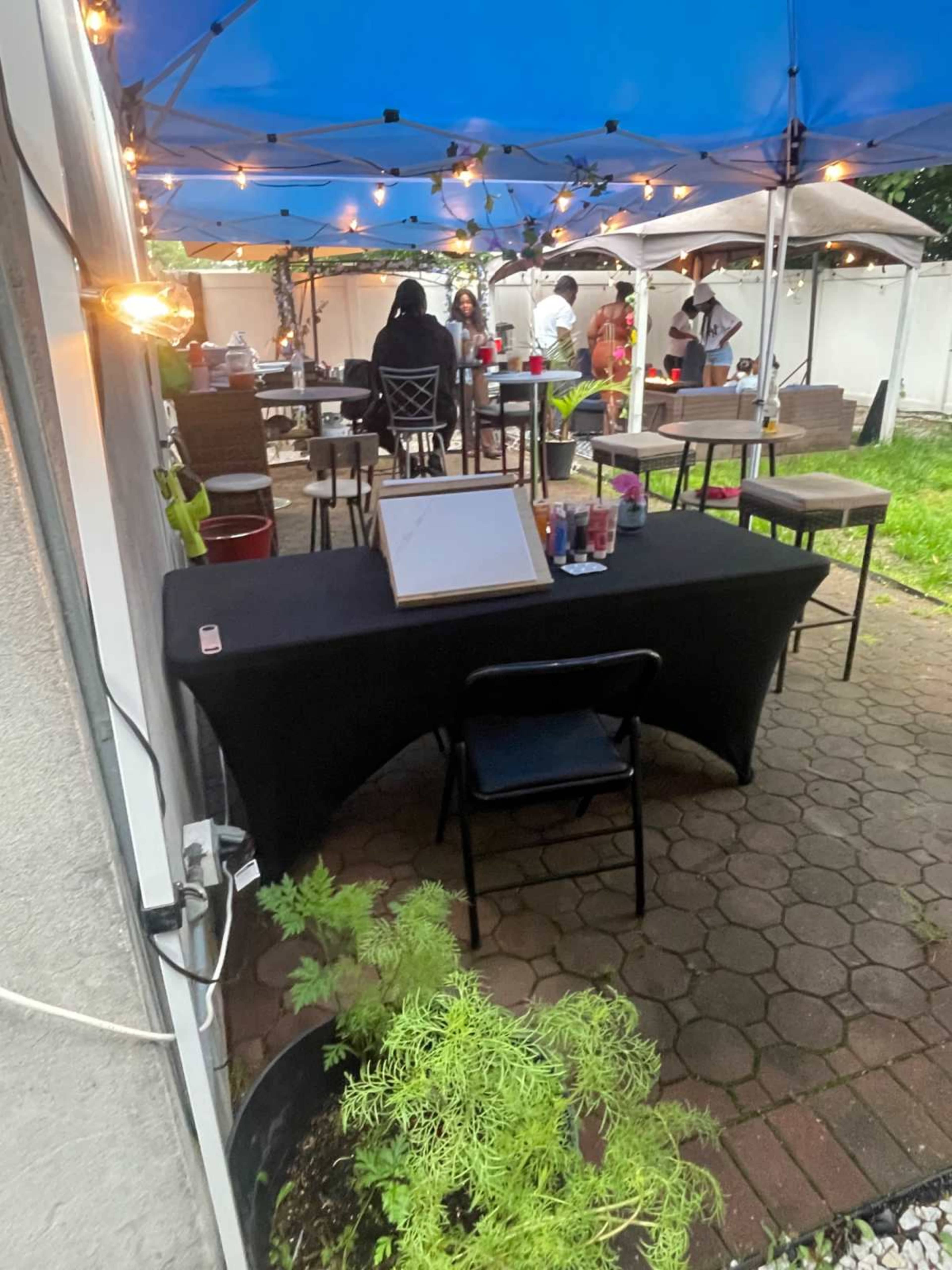 A covered outdoor space features tables and chairs set up for an event with string lights illuminating the area.