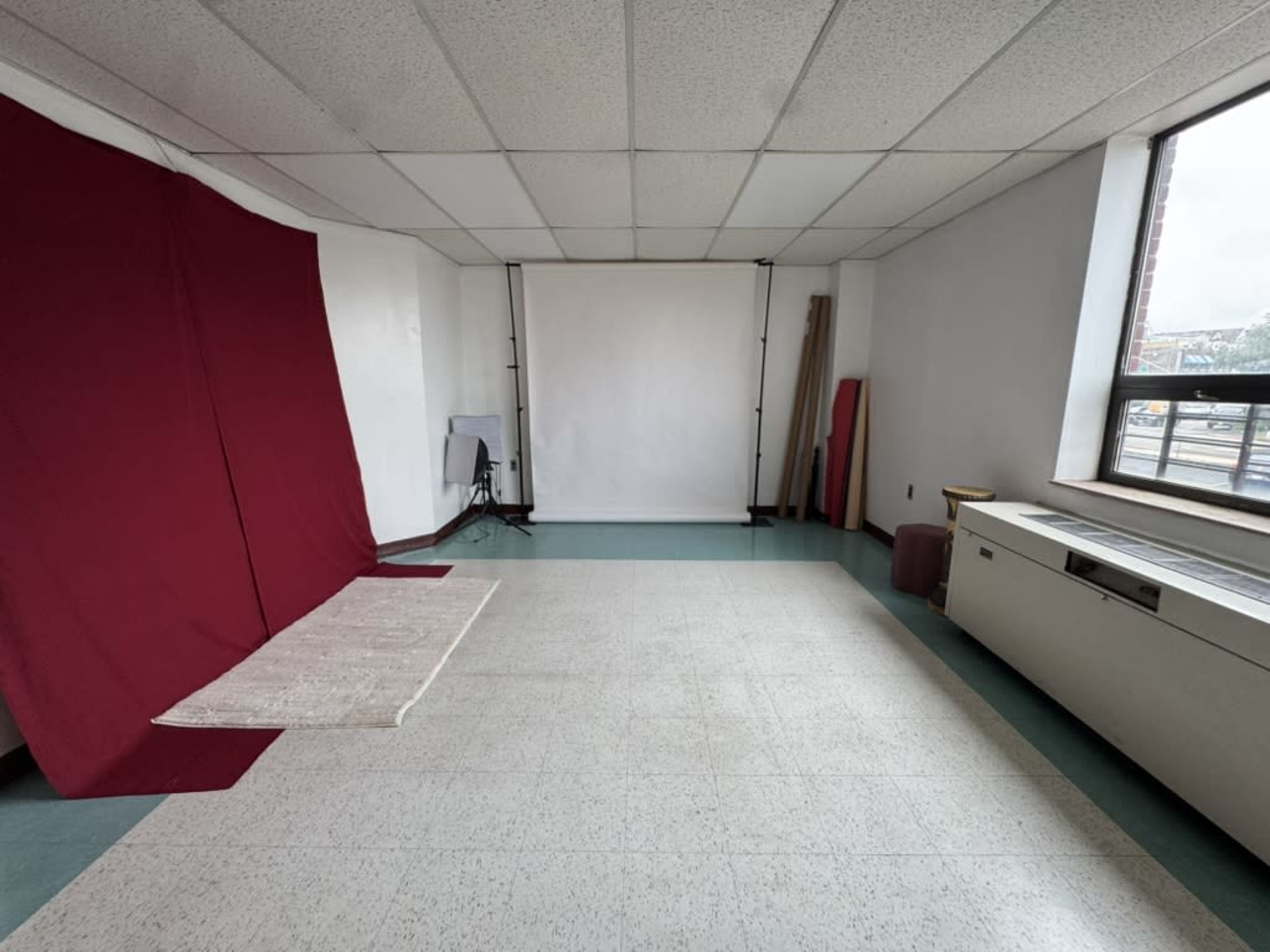 The image shows a spacious room with a red backdrop on one side, a plain white backdrop, and a light-colored rug on the floor.